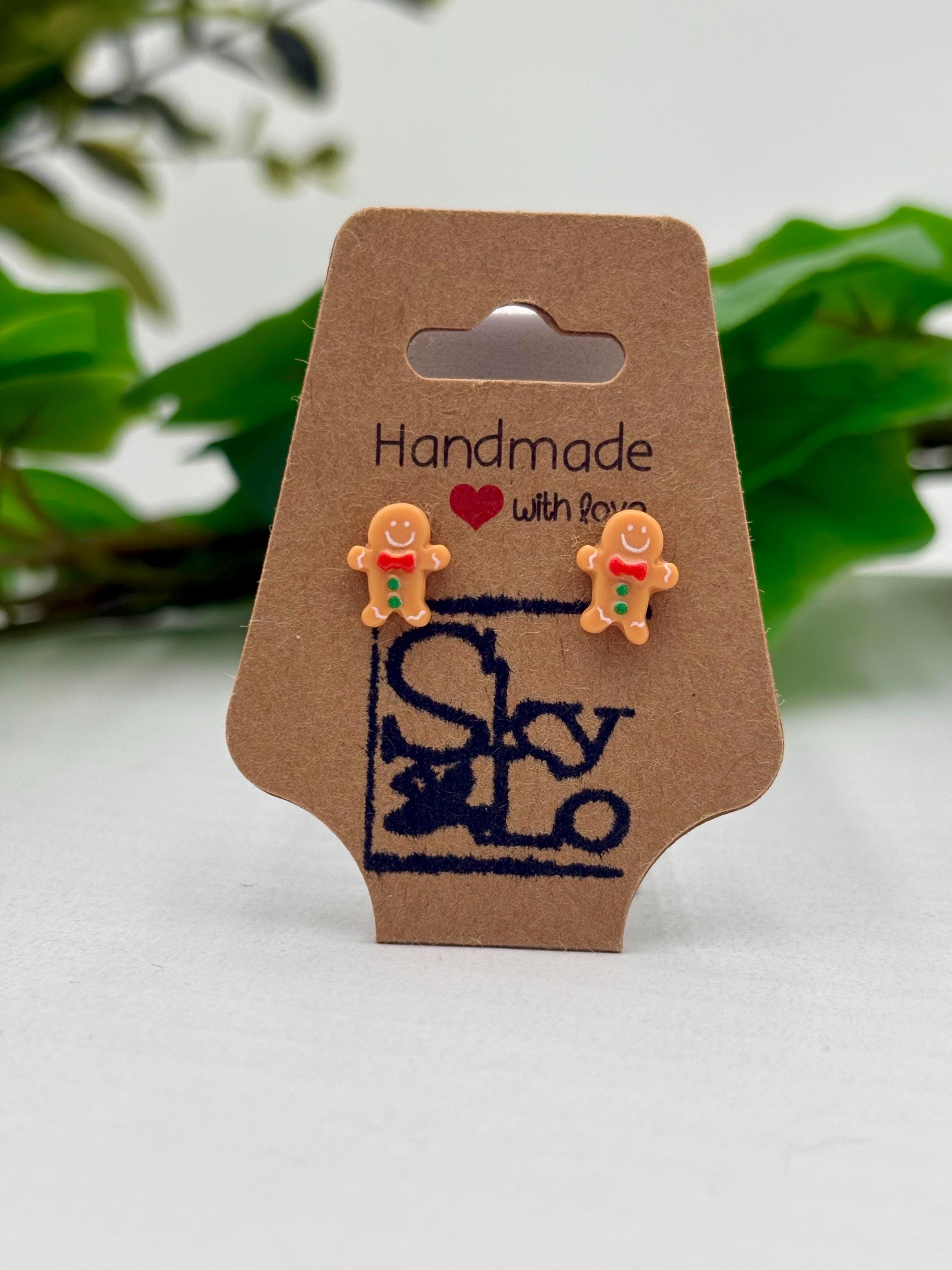 Handmade gingerbread man earrings on a brown card with 'SkyLo' branding, against a green leafy background.