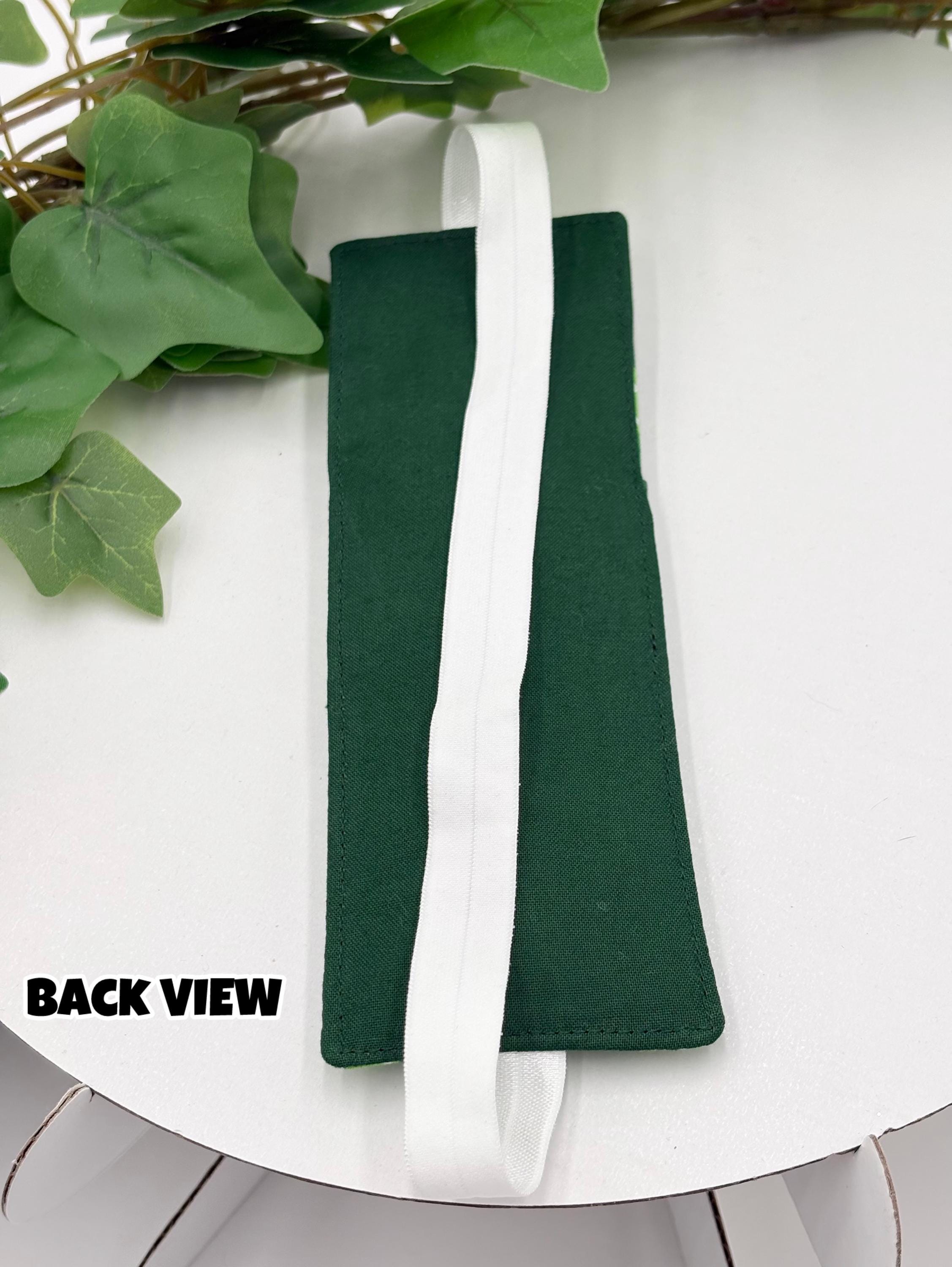 Green pen holder bookmark with white strap on a white background with green leaves.