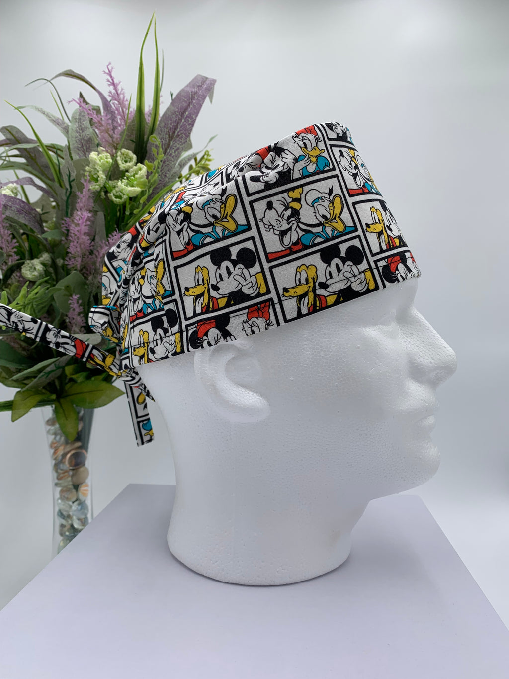 Mickey Mouse scrub cap on a mannequin head with a white background and flowers in the background