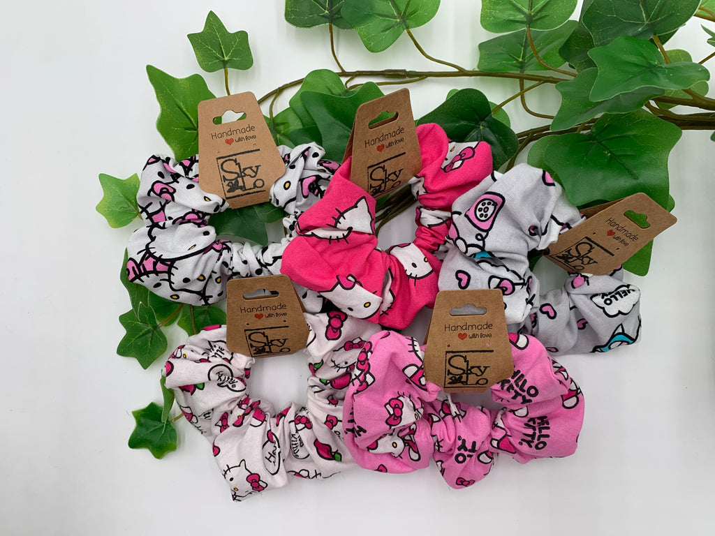 Set of 5 scrunchies with cute cat designs on a white background with green leaves.
