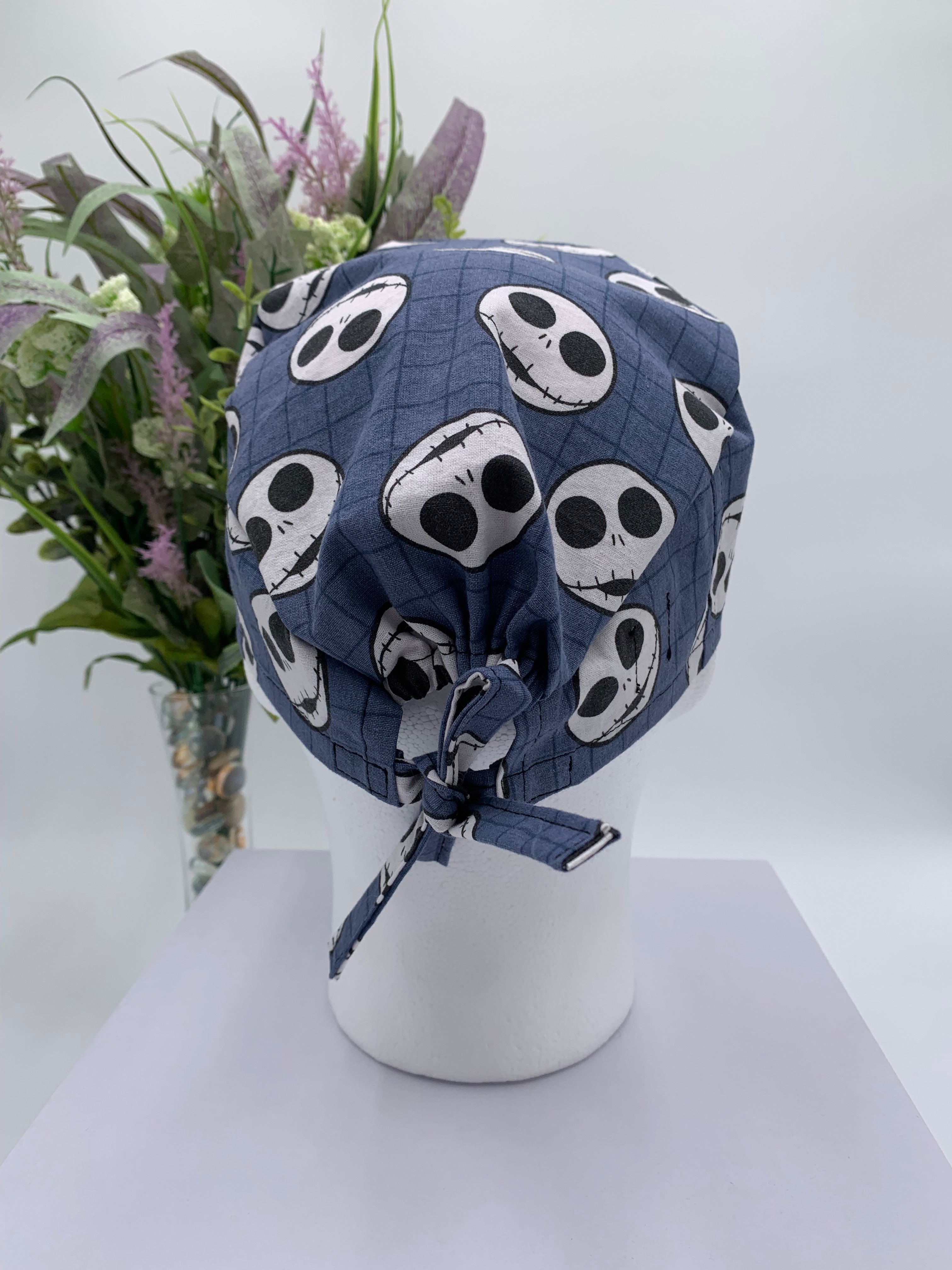 Mannequin head wearing a jack skellington scrub cap with a decorative plant in the background.