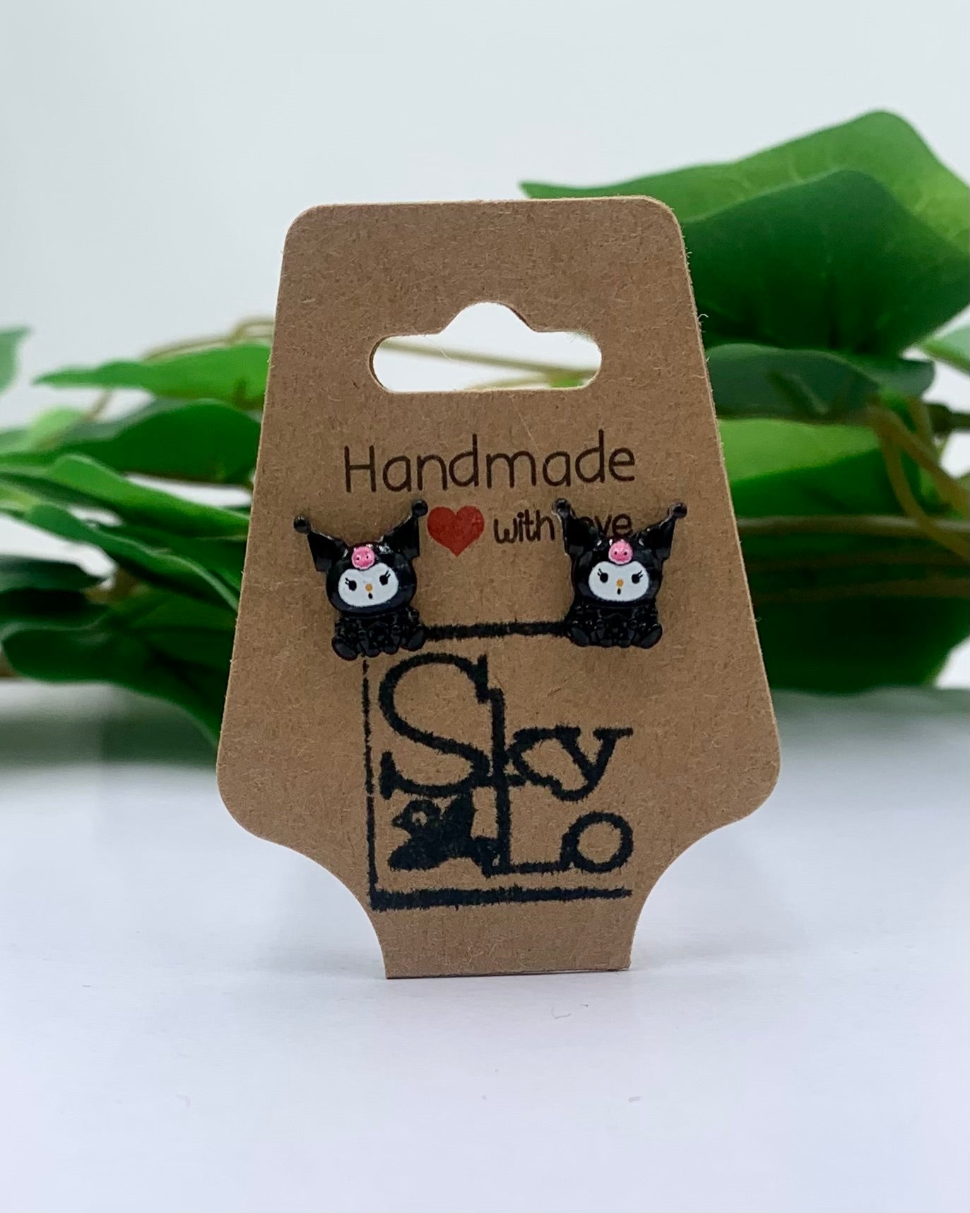 Pair of black cat-shaped earrings on a 'Handmade with Love Sky' branded card with green leaves in the background.