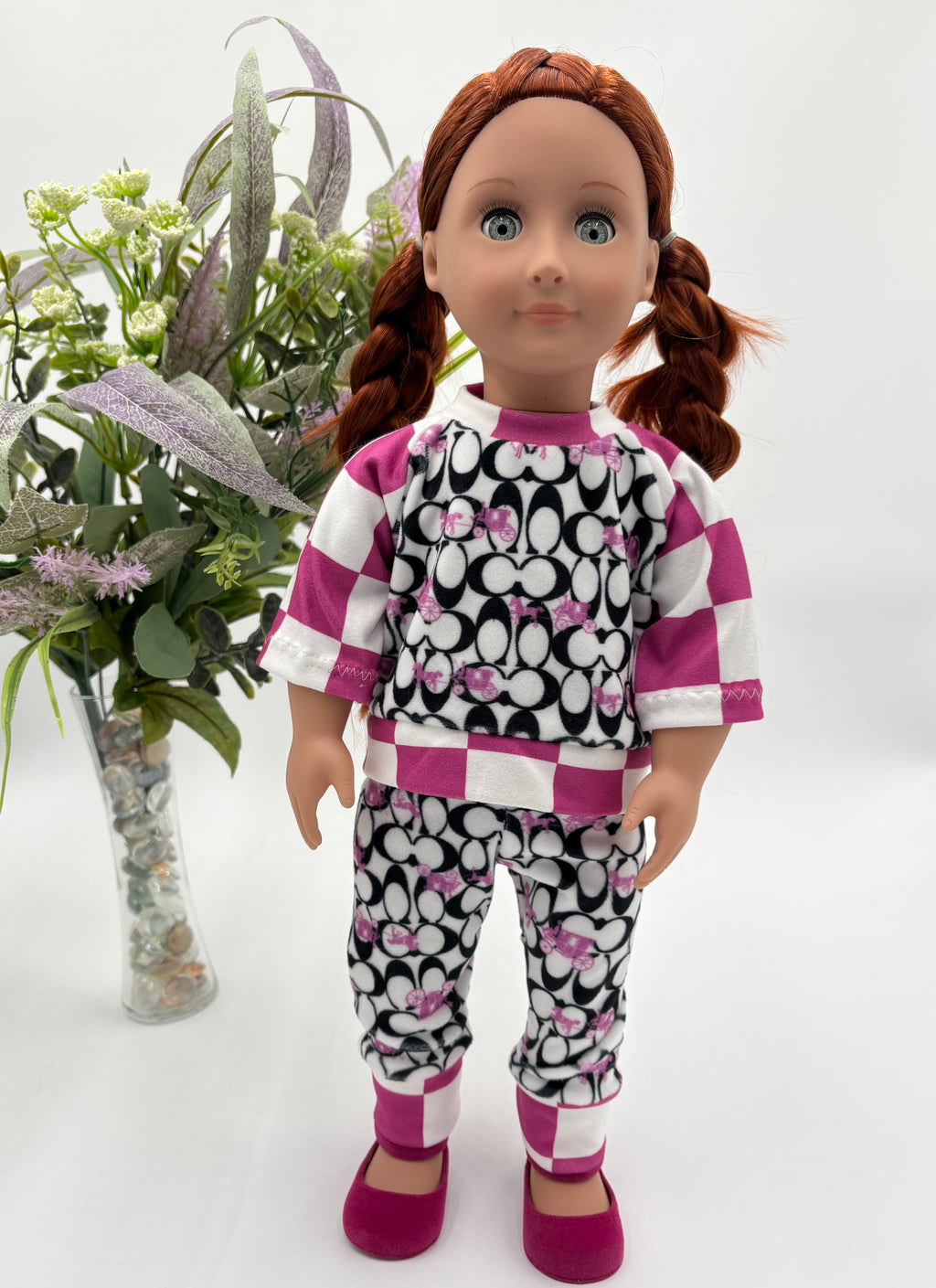 Doll wearing a black and white patterned outfit with pink accents, standing next to a vase of flowers.