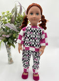Doll wearing a black and white patterned outfit with pink accents, standing next to a vase of flowers.