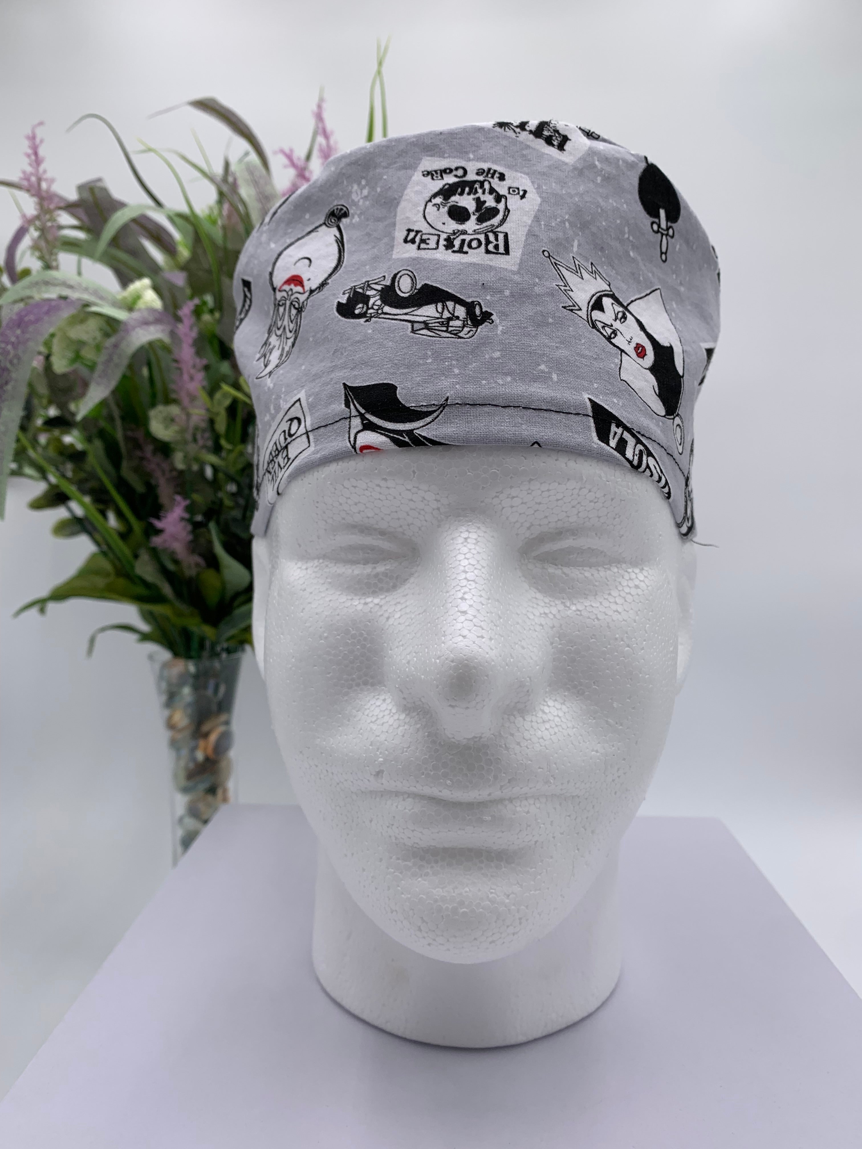 Gray scrub cap with black graphics on a mannequin head against a white background with flowers in the background