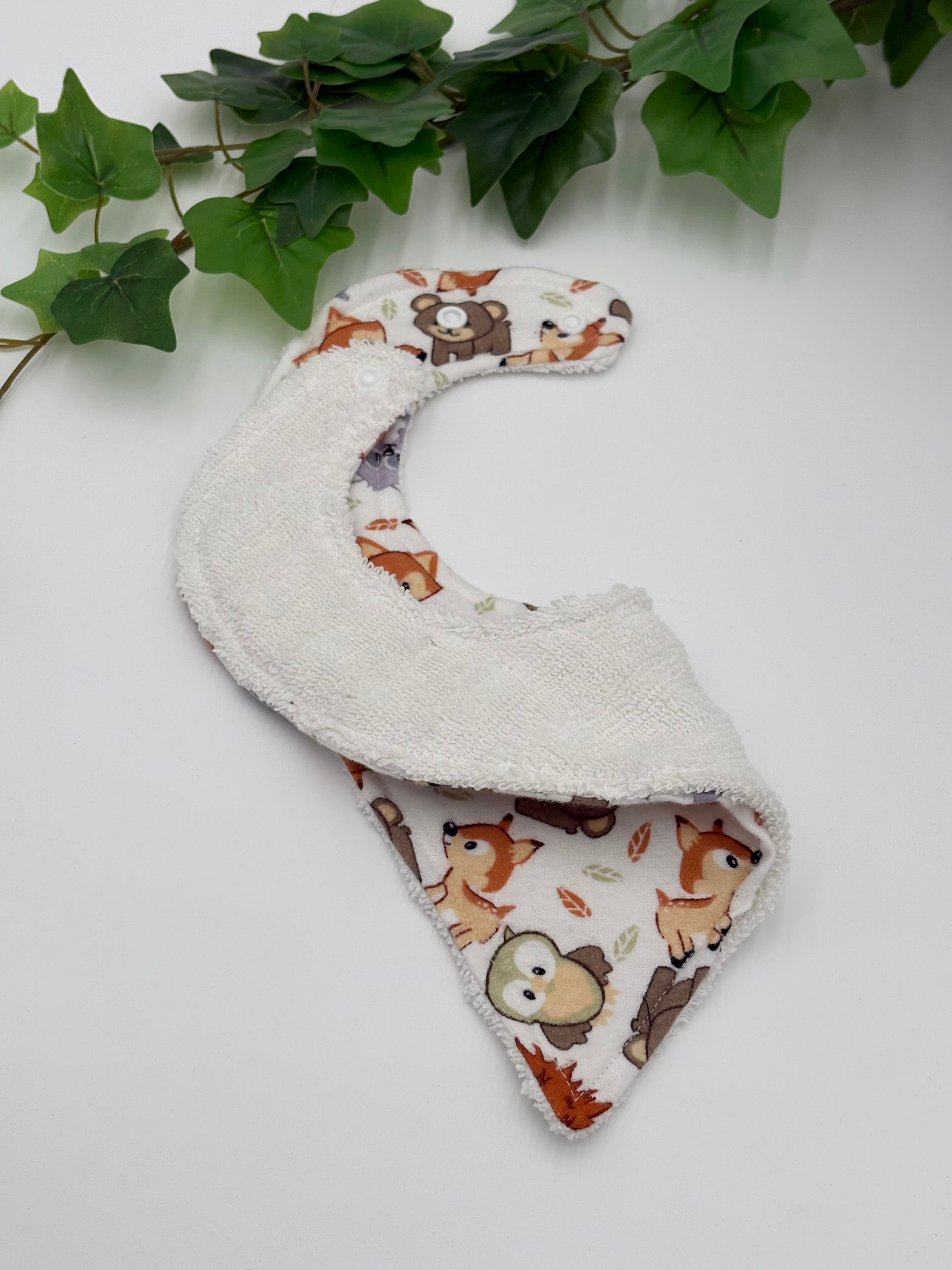 Baby bib with animal pattern showing the white backing on a white background with green leaves
