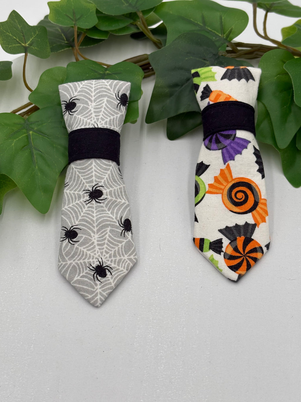 Two Halloween-themed bow ties on a white surface with green leaves.
