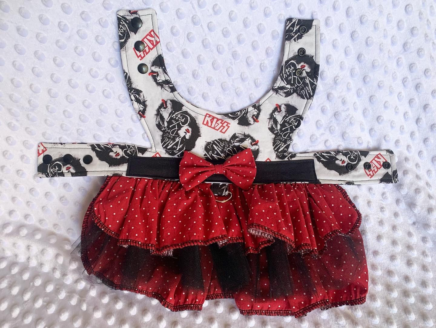 A red polka dot ruffle harness dress with heavy metal band design on it on a white textured background
