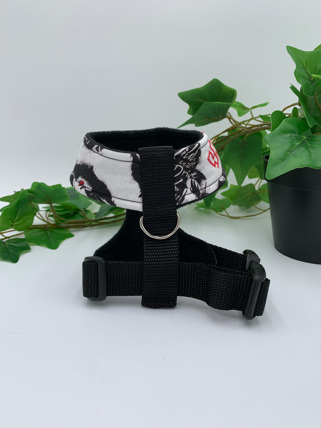 back view of a white heavy metal band pattern harness on a white background with a potted green plant