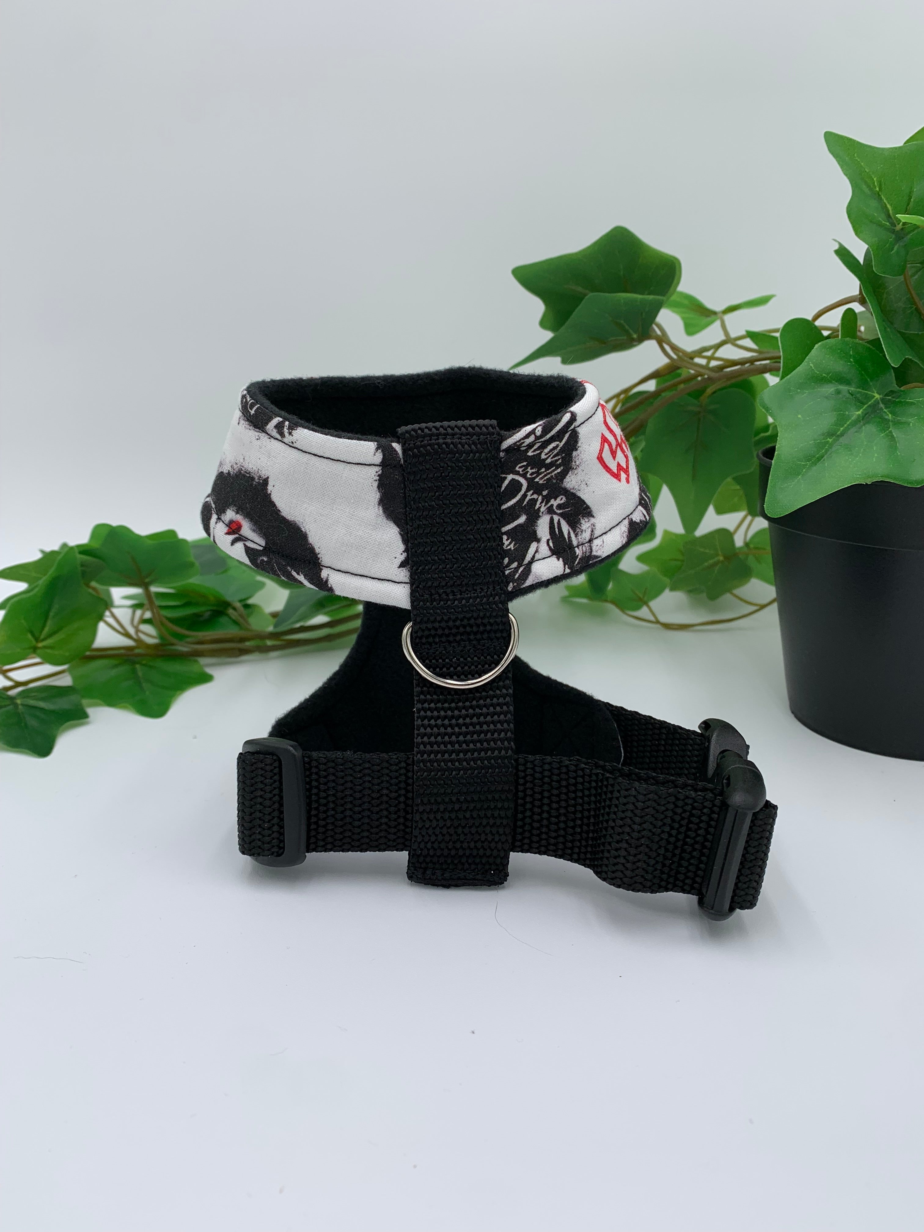 back view of a white heavy metal band pattern harness on a white background with a potted green plant