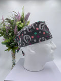 Gray polka dot nightmare before Christmas scrub cap on a mannequin head with flowers, against a white background