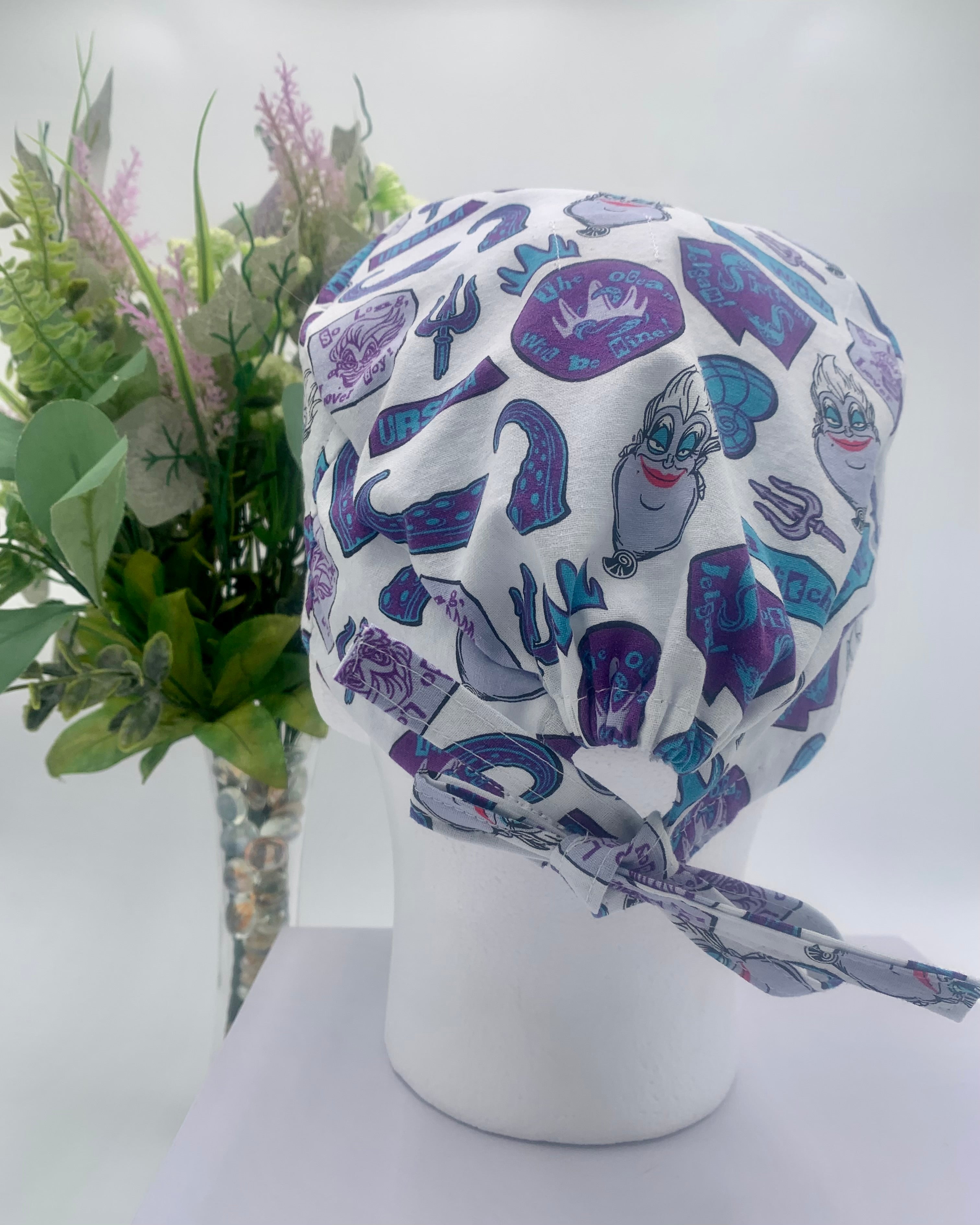 Colorful Little Mermaid Ursula scrub cap on a mannequin head with flowers, against a white background
