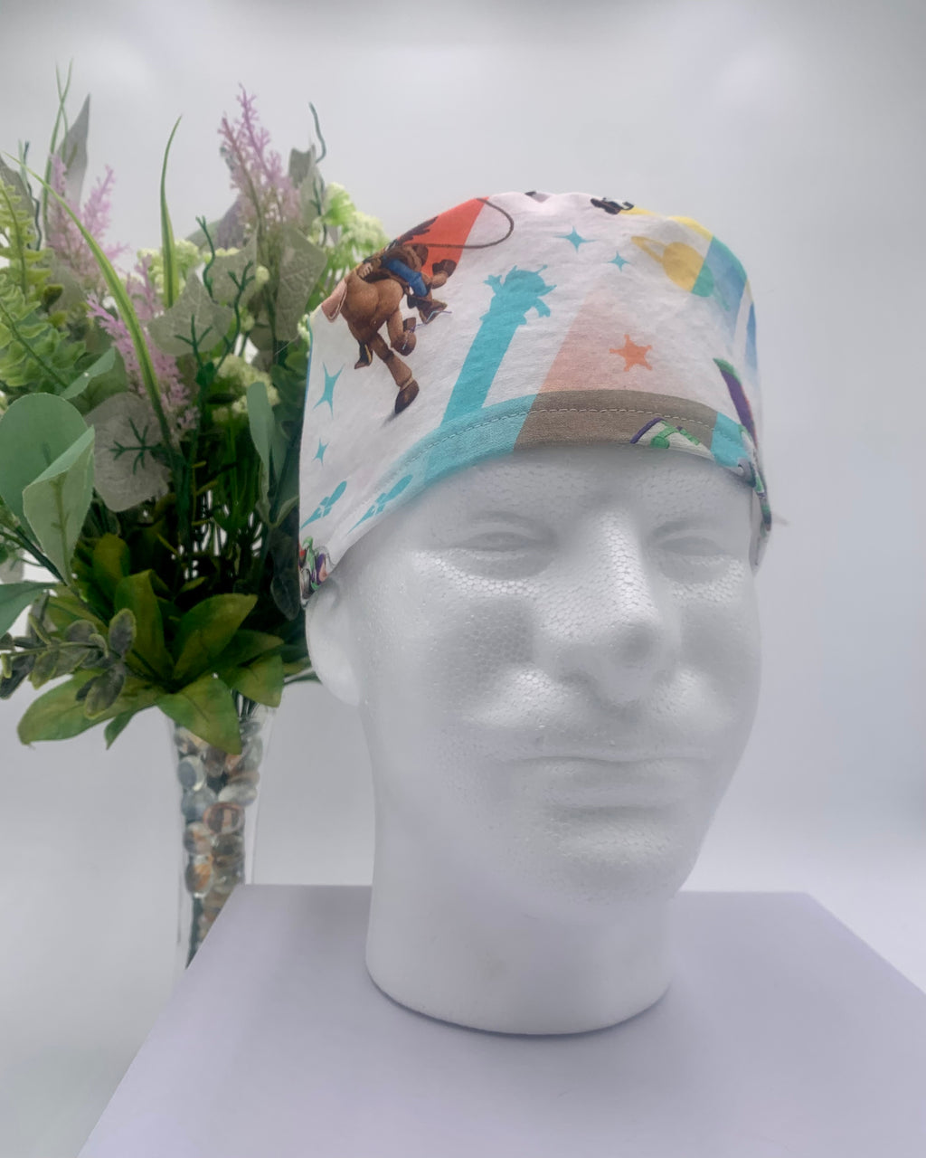 Colorful Toy Story scrub cap on a mannequin head with flowers, against a white background