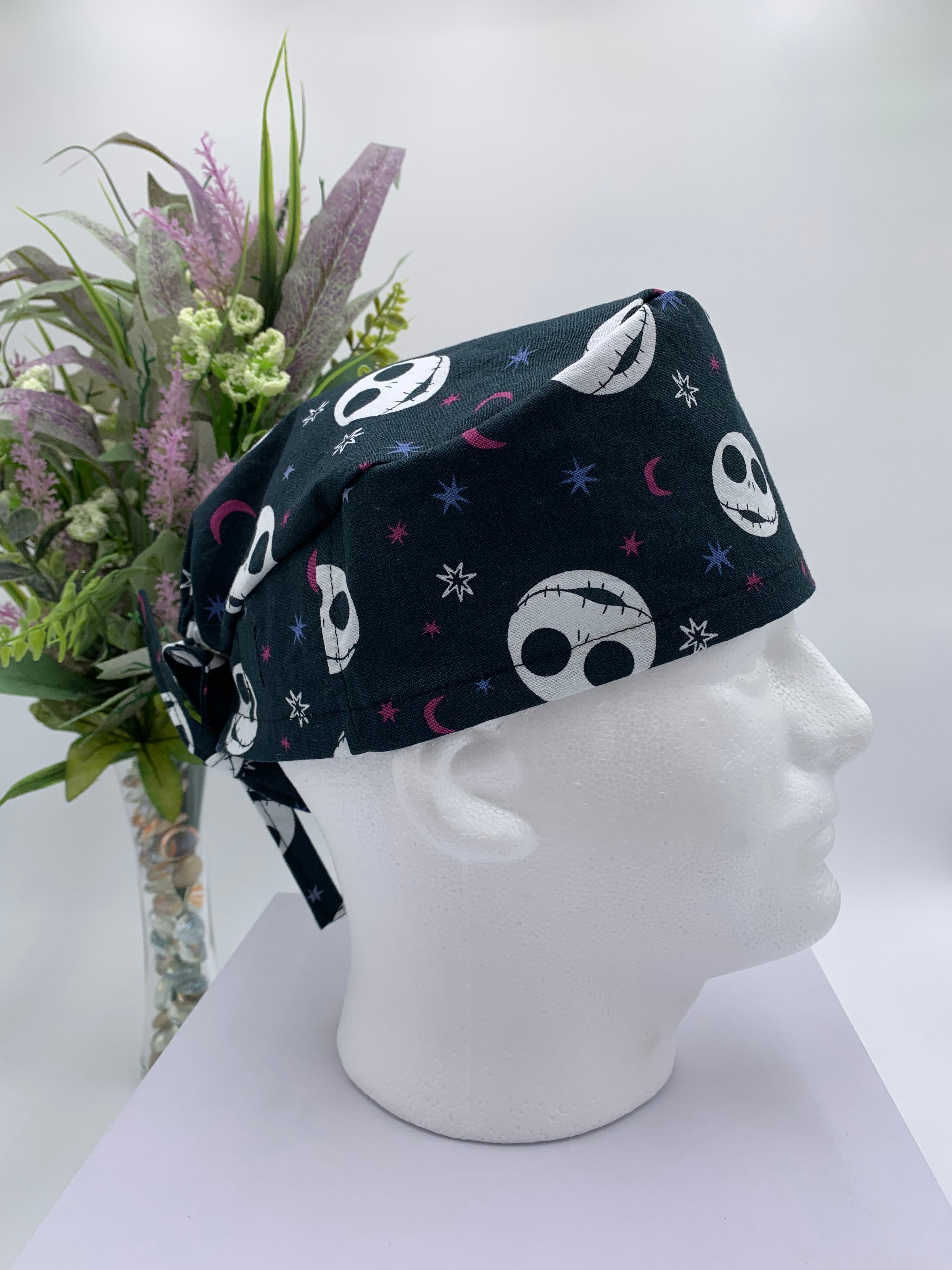 Mannequin head wearing a jack skellington scrub cap with a decorative plant in the background.