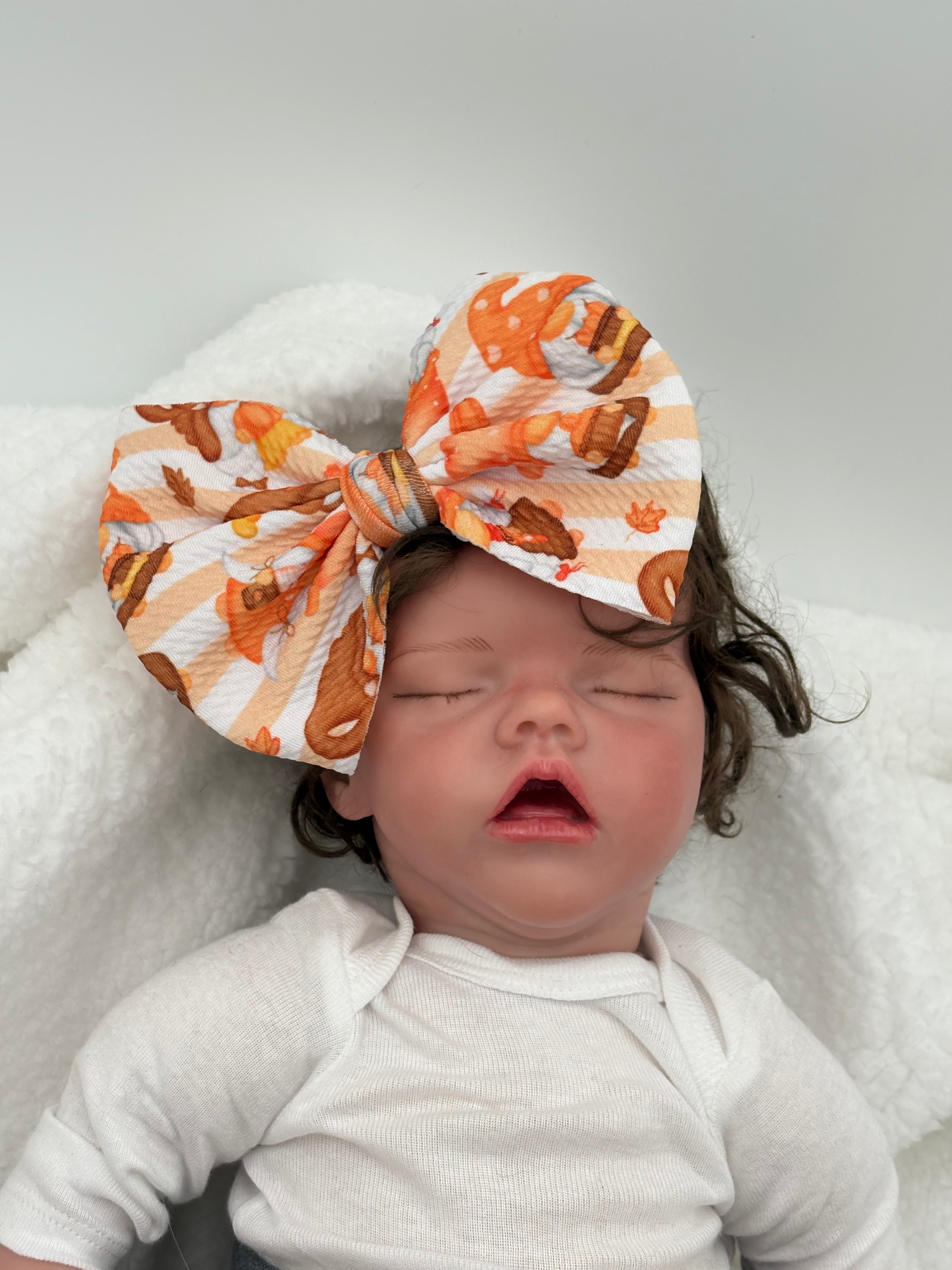 baby doll wearing a Autumn gnomes themed big bow nylon headband on a white background