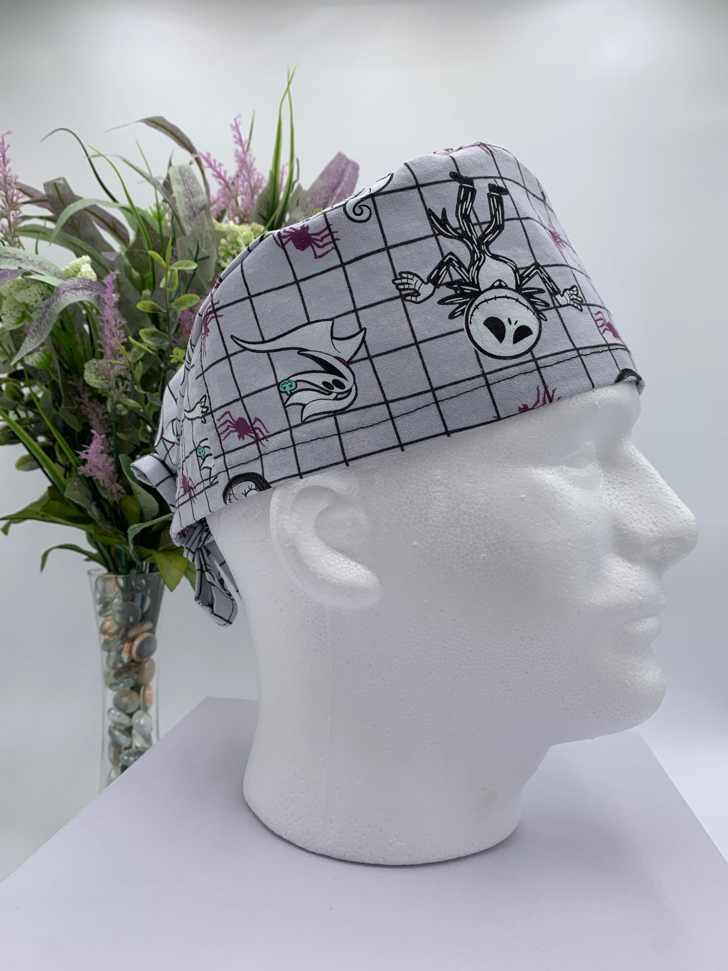 Mannequin head wearing a nightmare before christmas scrub cap with a decorative plant in the background.