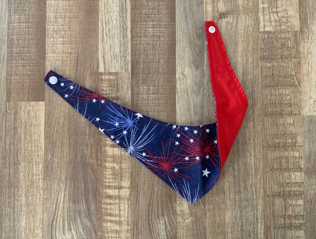 Blue with light blue and red fireworks with white stars 4th of july themed pet bandana showing the back with red fabric on a wooden floor