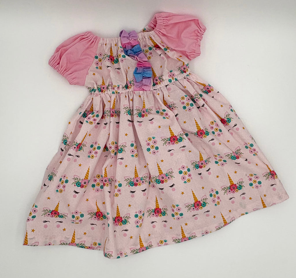 Pink children's dress with unicorn and flower pattern on a white background