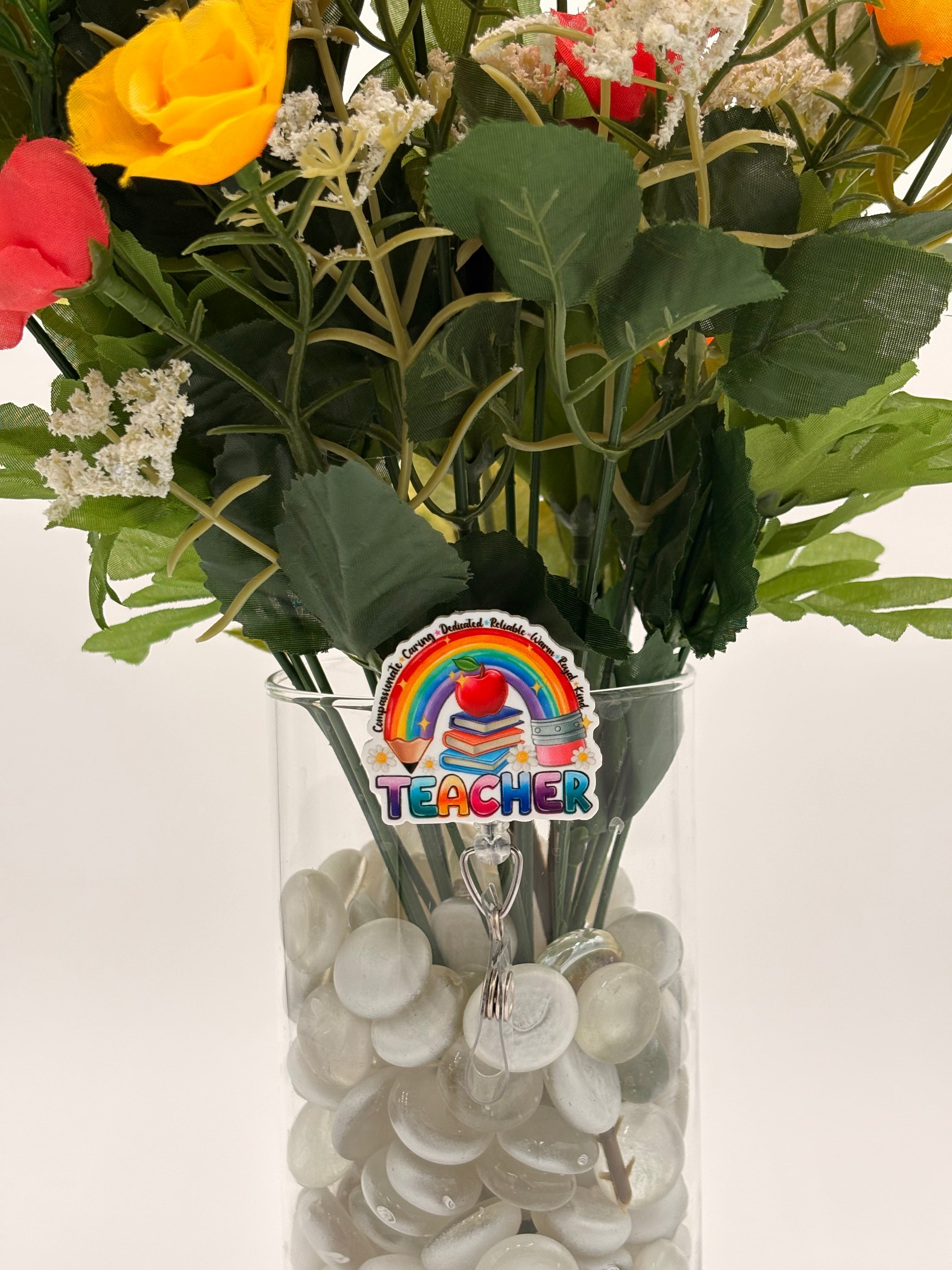 Bouquet of flowers with a pencil rainbow with text "Teacher" badge holder in a clear vase on a white background