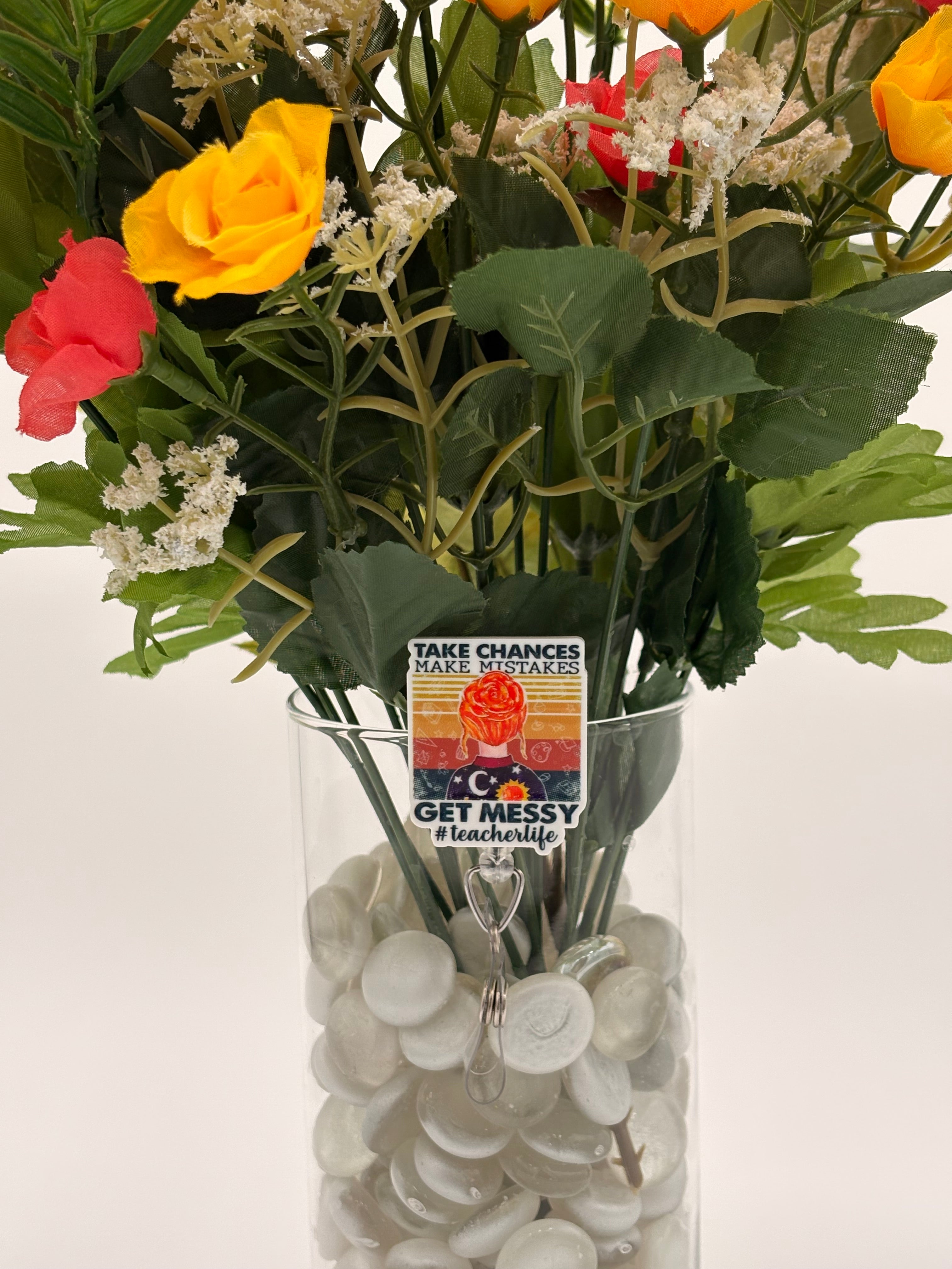 Bouquet of flowers with a red headed woman with text "Take chances make mistakes get messy #teacherlife" badge holder in a clear vase on a white background