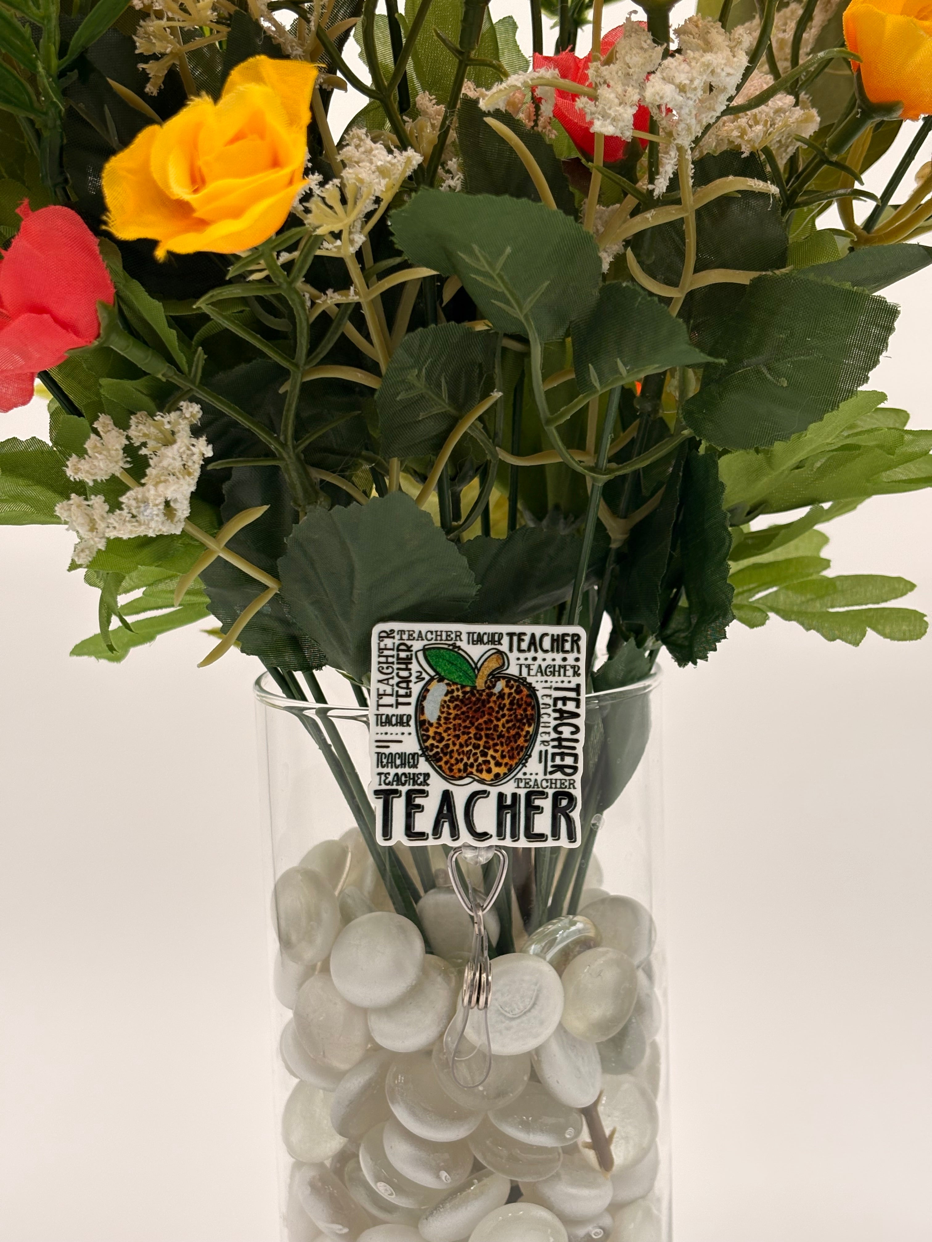 Bouquet of flowers with leopard print apple with text "Teacher" badge holder in a clear vase on a white background