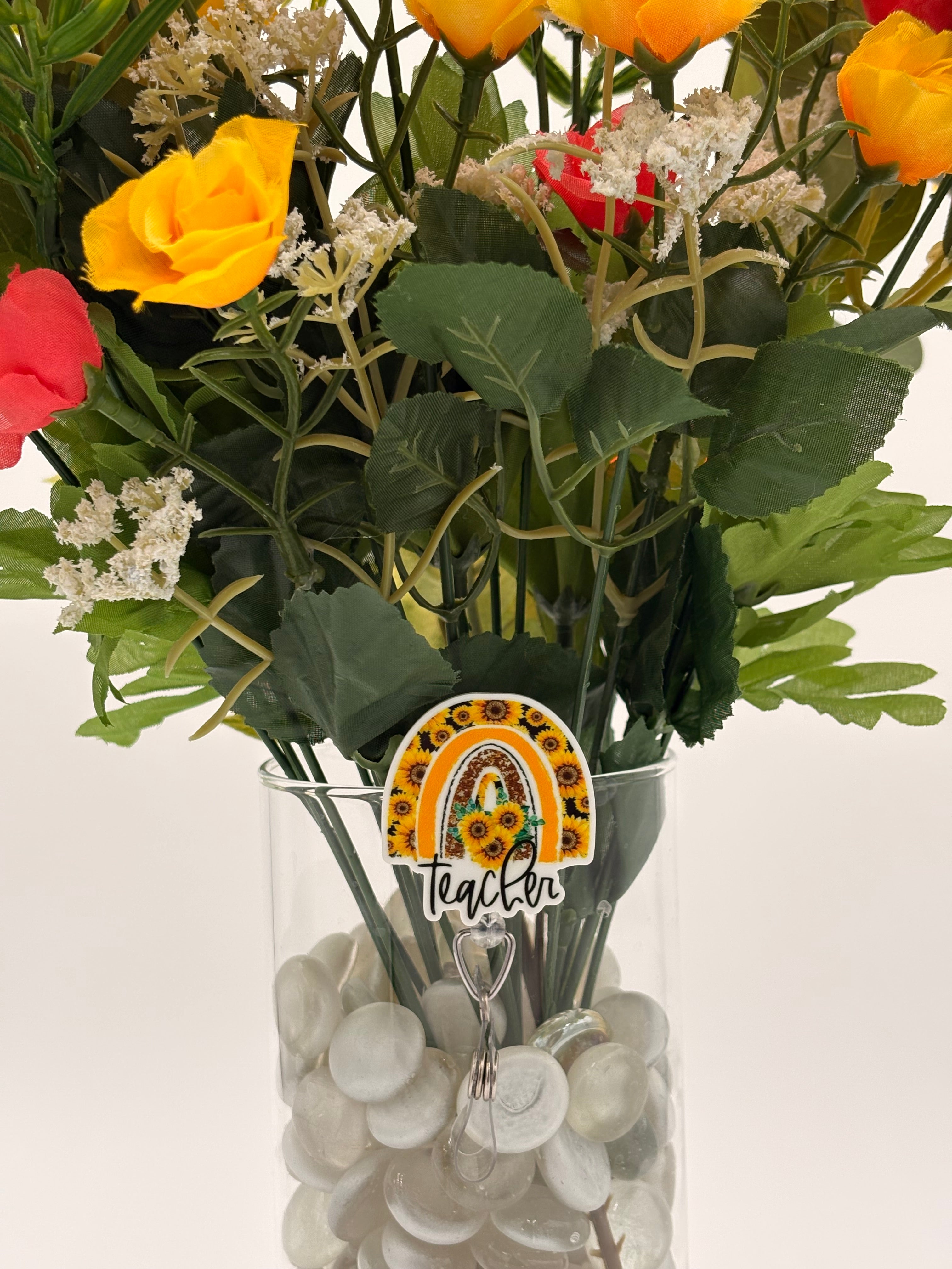 Bouquet of flowers with a rainbow sunflower with text "Teacher" badge holder in a clear vase on a white background