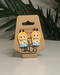 Princess shaped earrings with a Kraft branded label on a neutral background with a green plant. 
