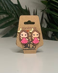 Princess shaped earrings with a Kraft branded label on a neutral background with a green plant. 