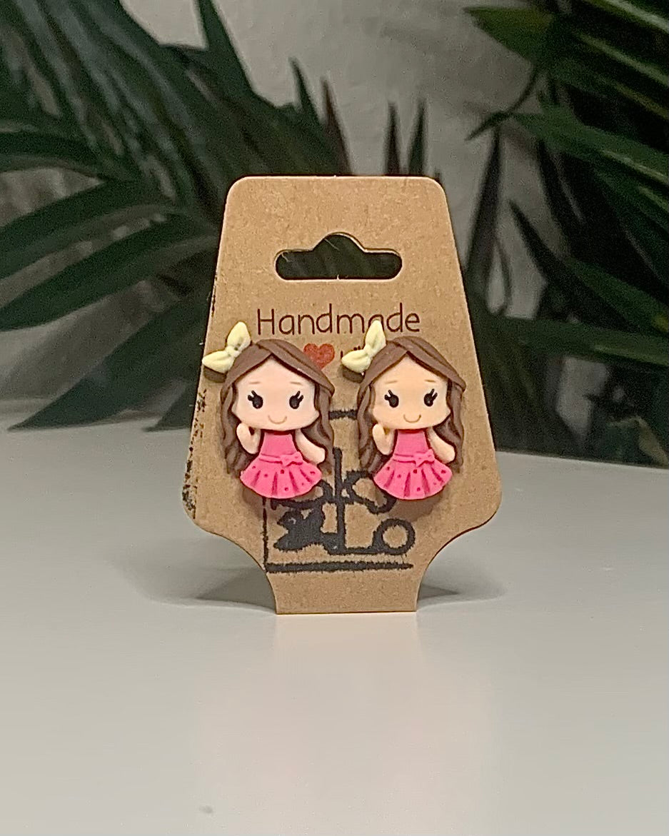 Princess shaped earrings with a Kraft branded label on a neutral background with a green plant. 