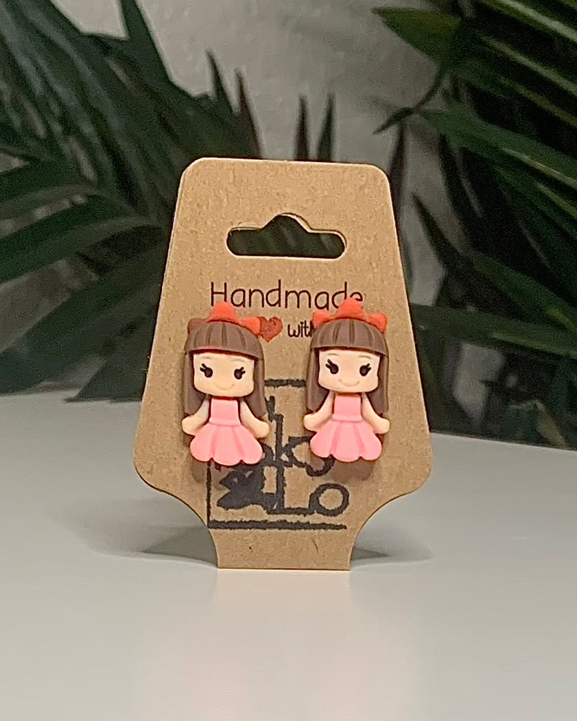 Princess shaped earrings with a Kraft branded label on a neutral background with a green plant. 