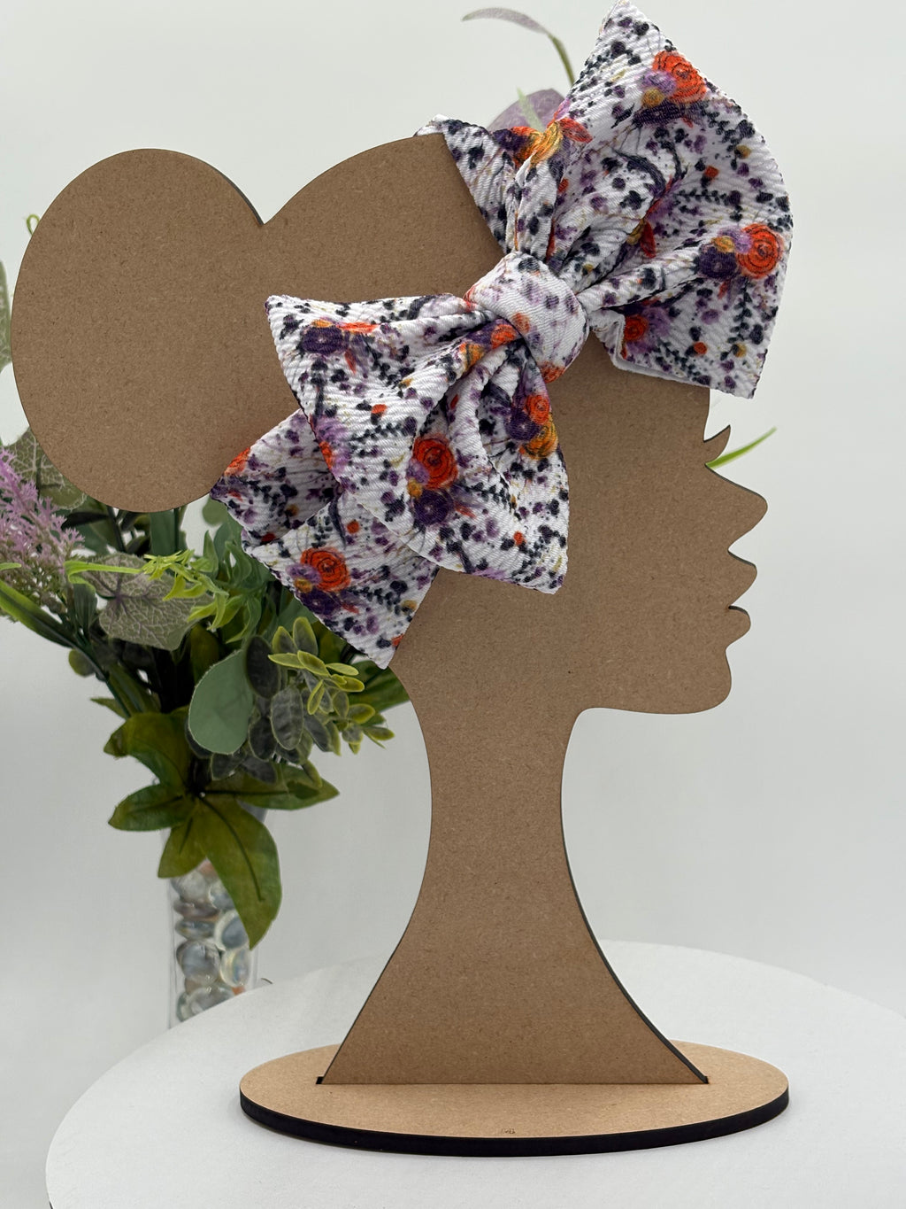 Autumn colored floral themed big bow headband on a mannequin head with a white background and greenery 