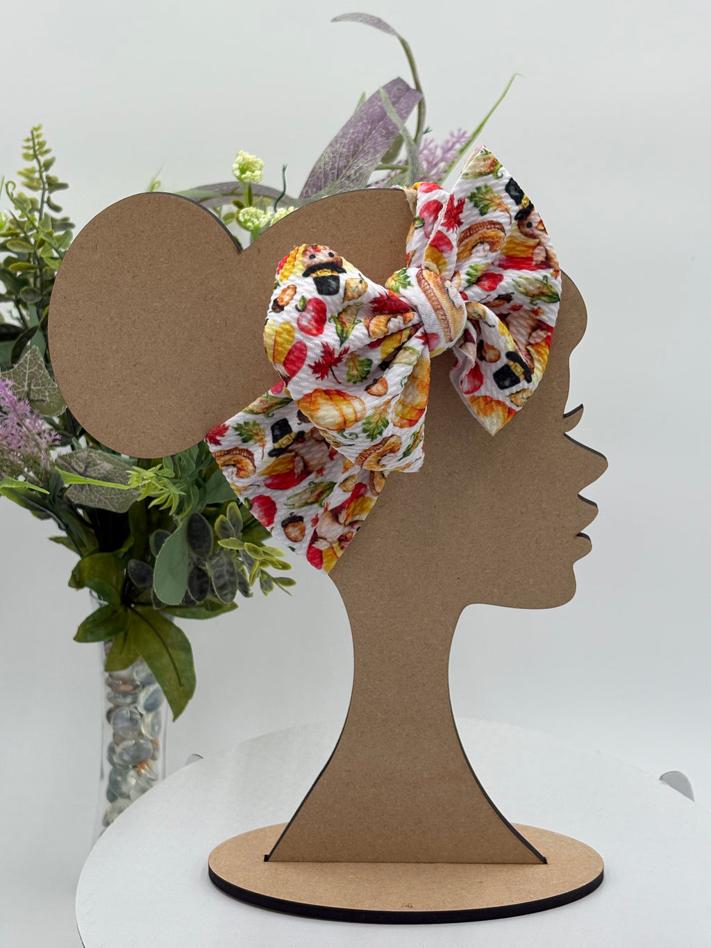 Colorful thanksgiving themed big bow headband on a mannequin head with a white background and greenery 
