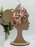 Colorful thanksgiving themed big bow headband on a mannequin head with a white background and greenery 