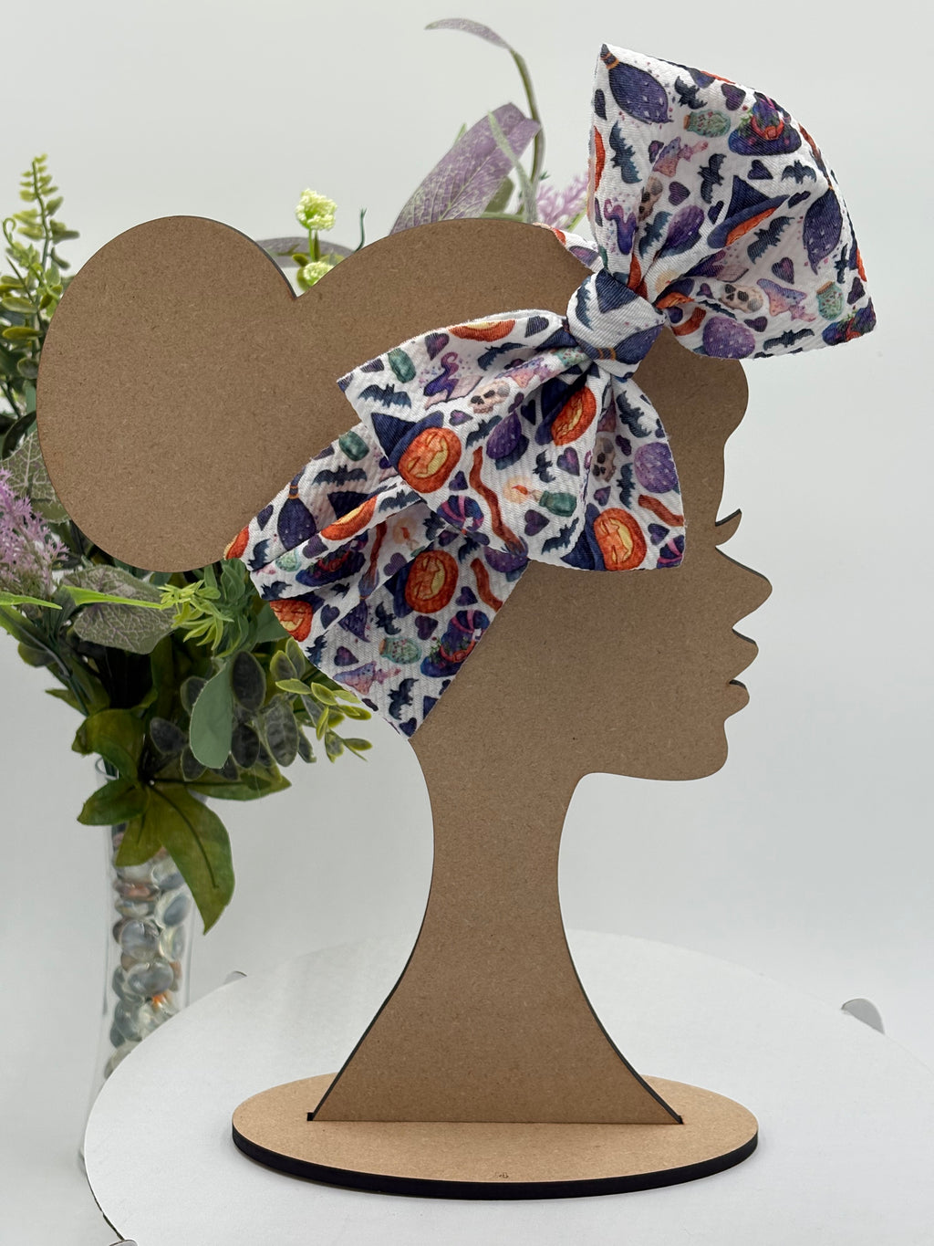 Colorful halloween themed big bow headband on a mannequin head with a white background and greenery 