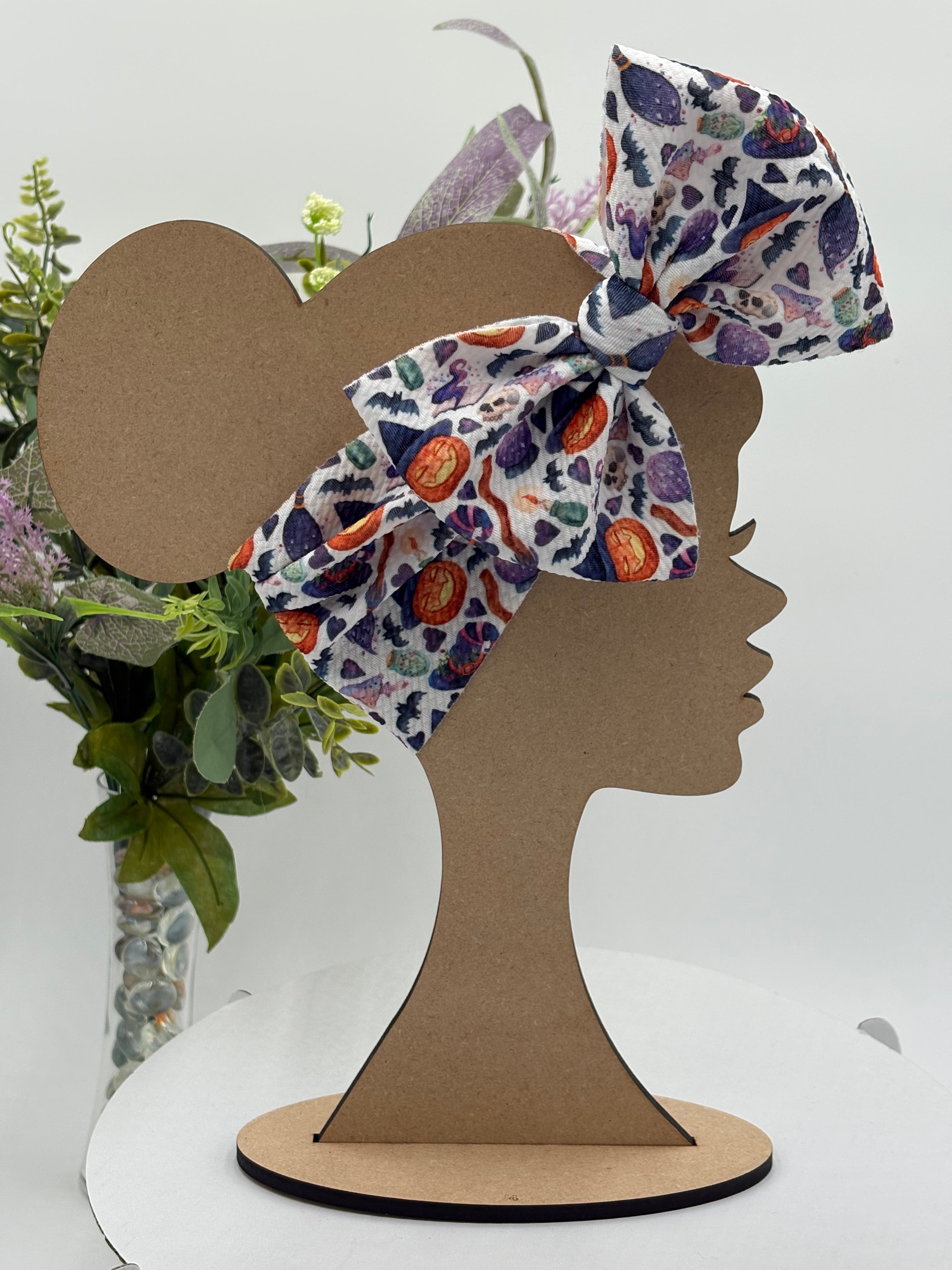 Colorful halloween themed big bow headband on a mannequin head with a white background and greenery 