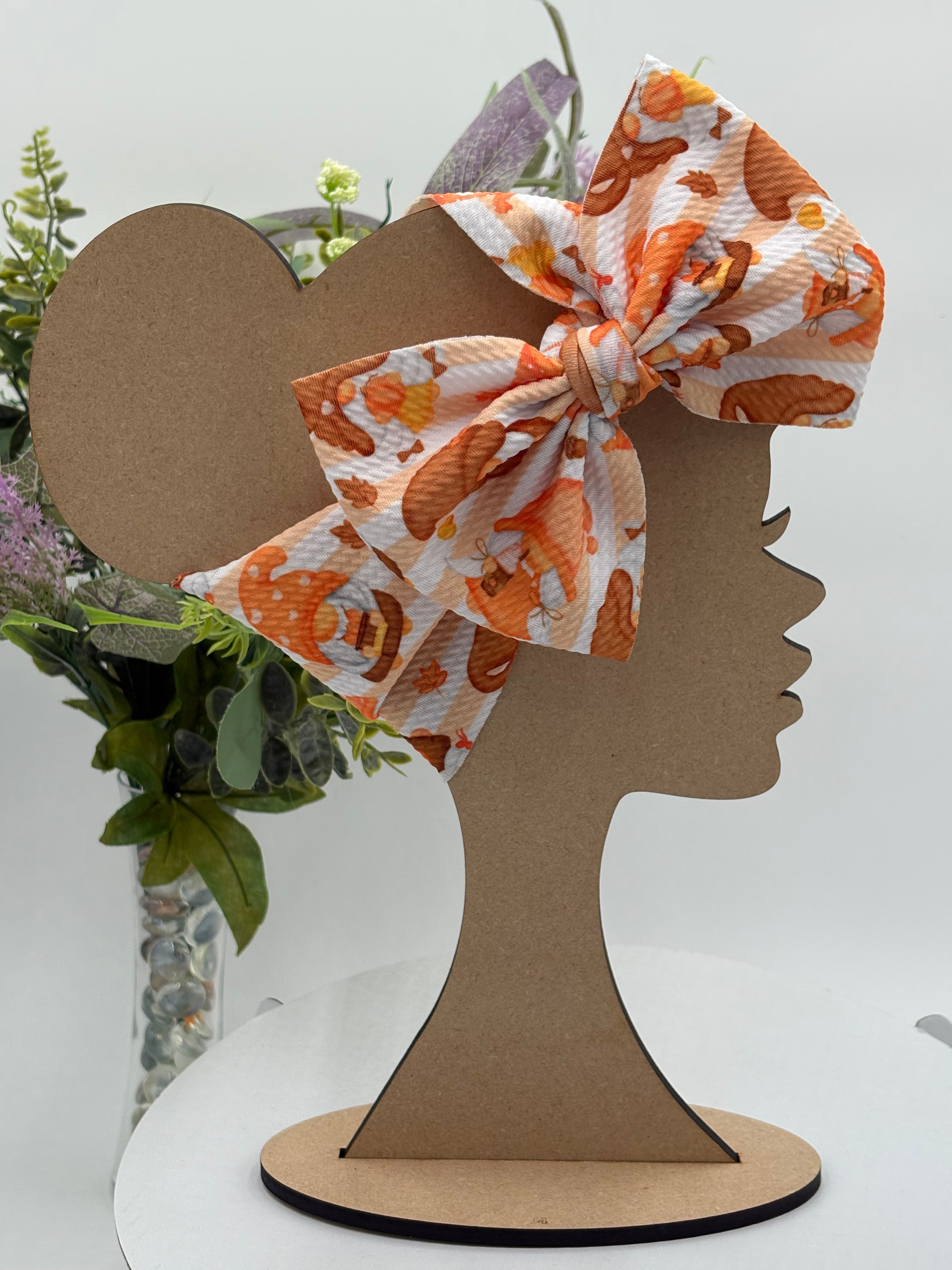 Autumn gnome themed big bow headband on a mannequin head with a white background and greenery 