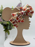 Colorful Apple pie themed big bow headband on a mannequin head with a white background and greenery 