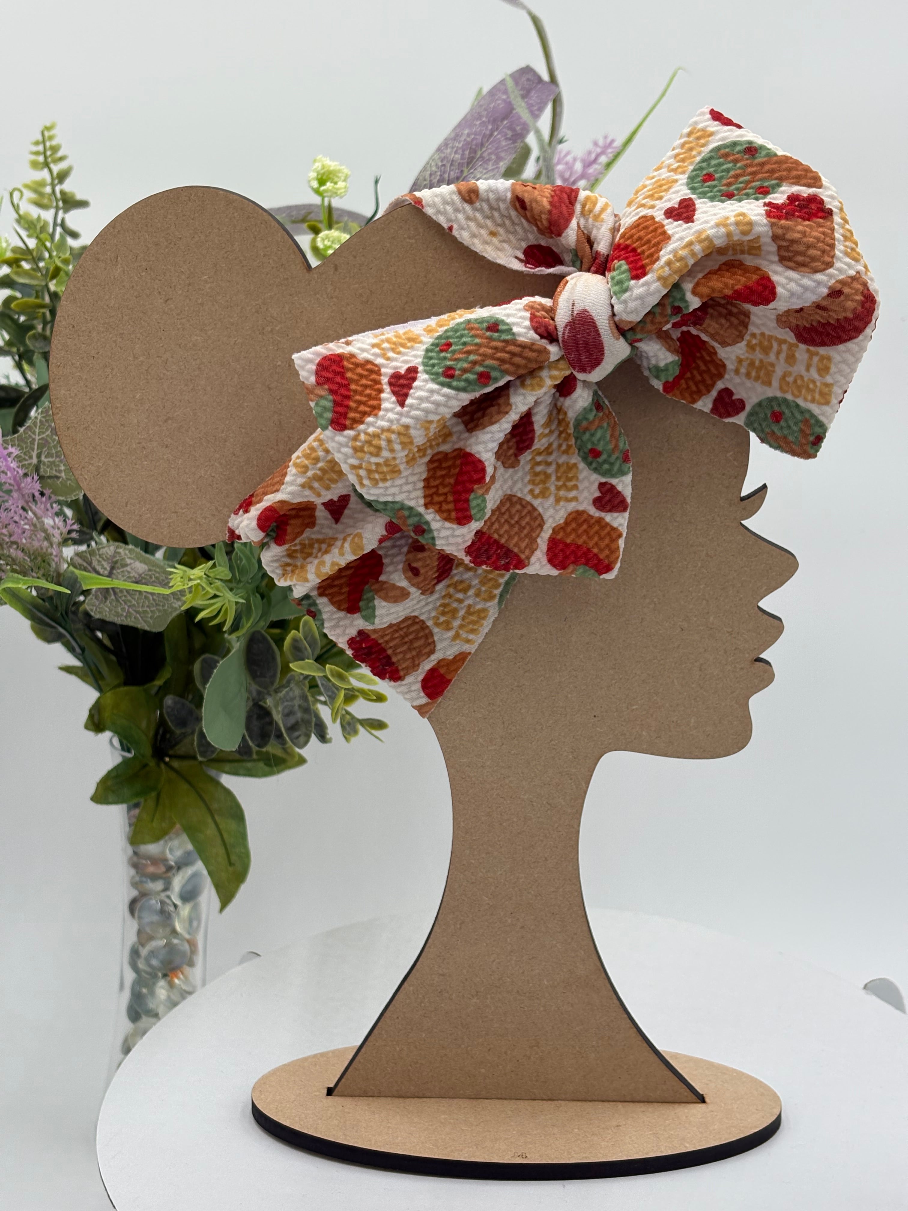 Colorful Apple pie themed big bow headband on a mannequin head with a white background and greenery 