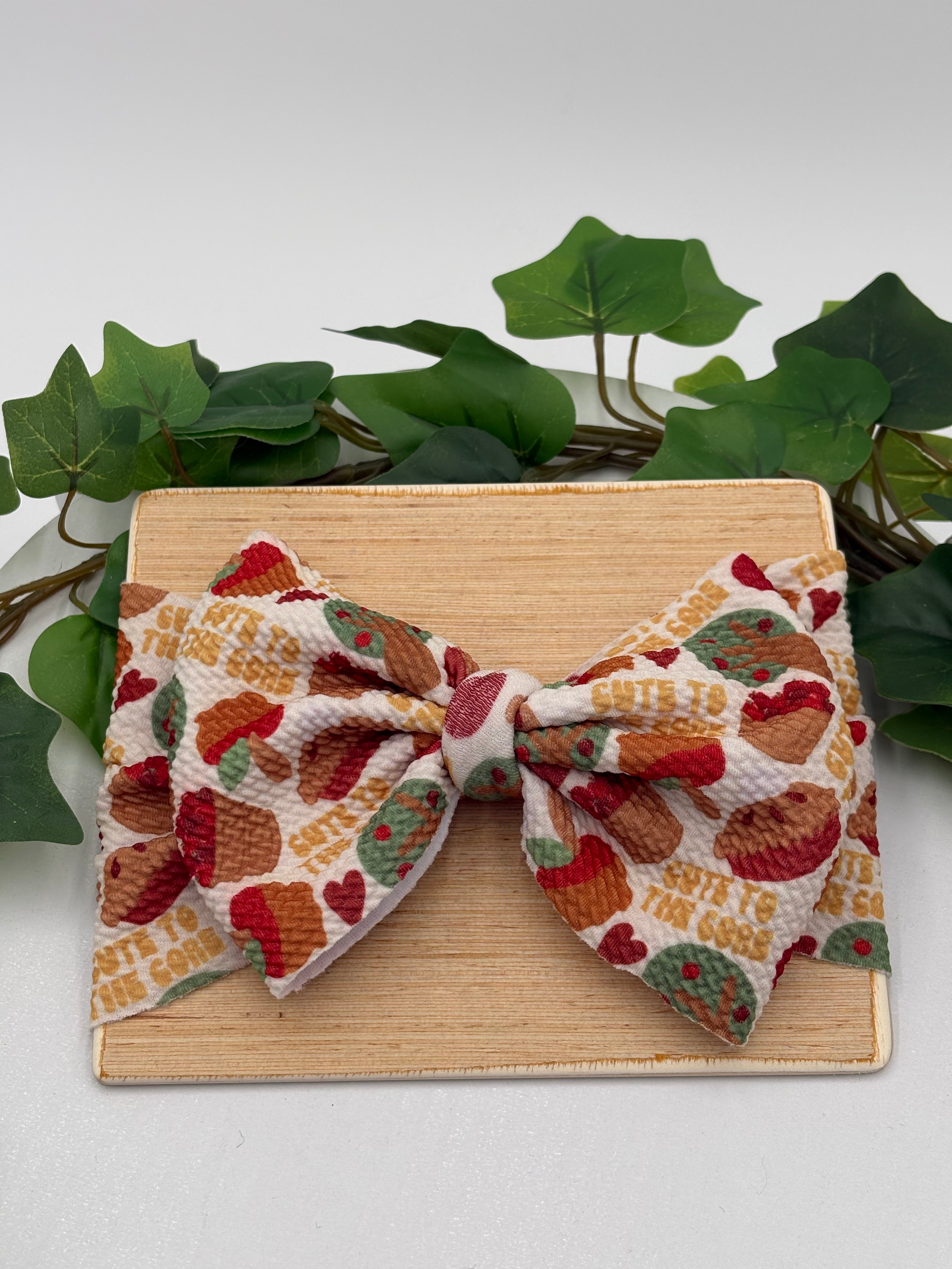Colorful Apple pie themed big bow headband on a wooden board with a white background and greenery 