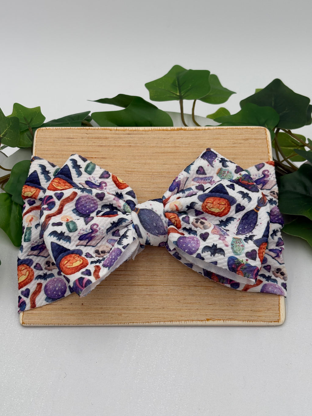 Colorful halloween themed big bow headband on a wooden board with a white background and greenery 