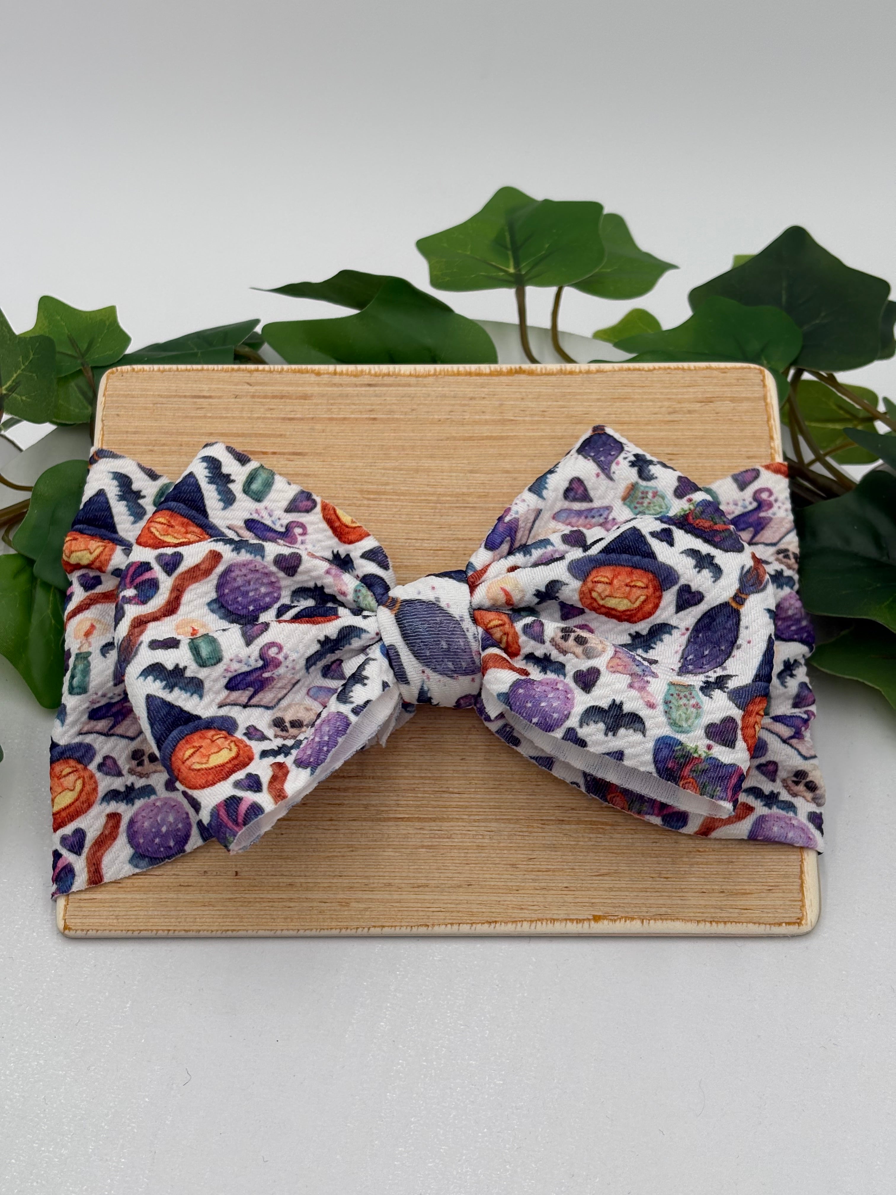 Colorful halloween themed big bow headband on a wooden board with a white background and greenery 