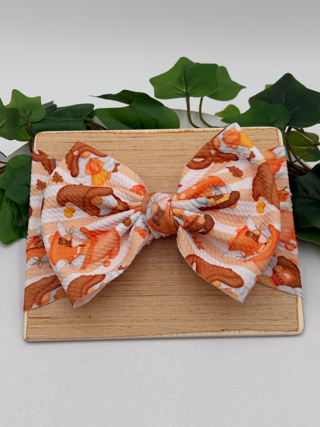 Autumn gnome themed big bow headband on a wooden board with a white background and greenery 