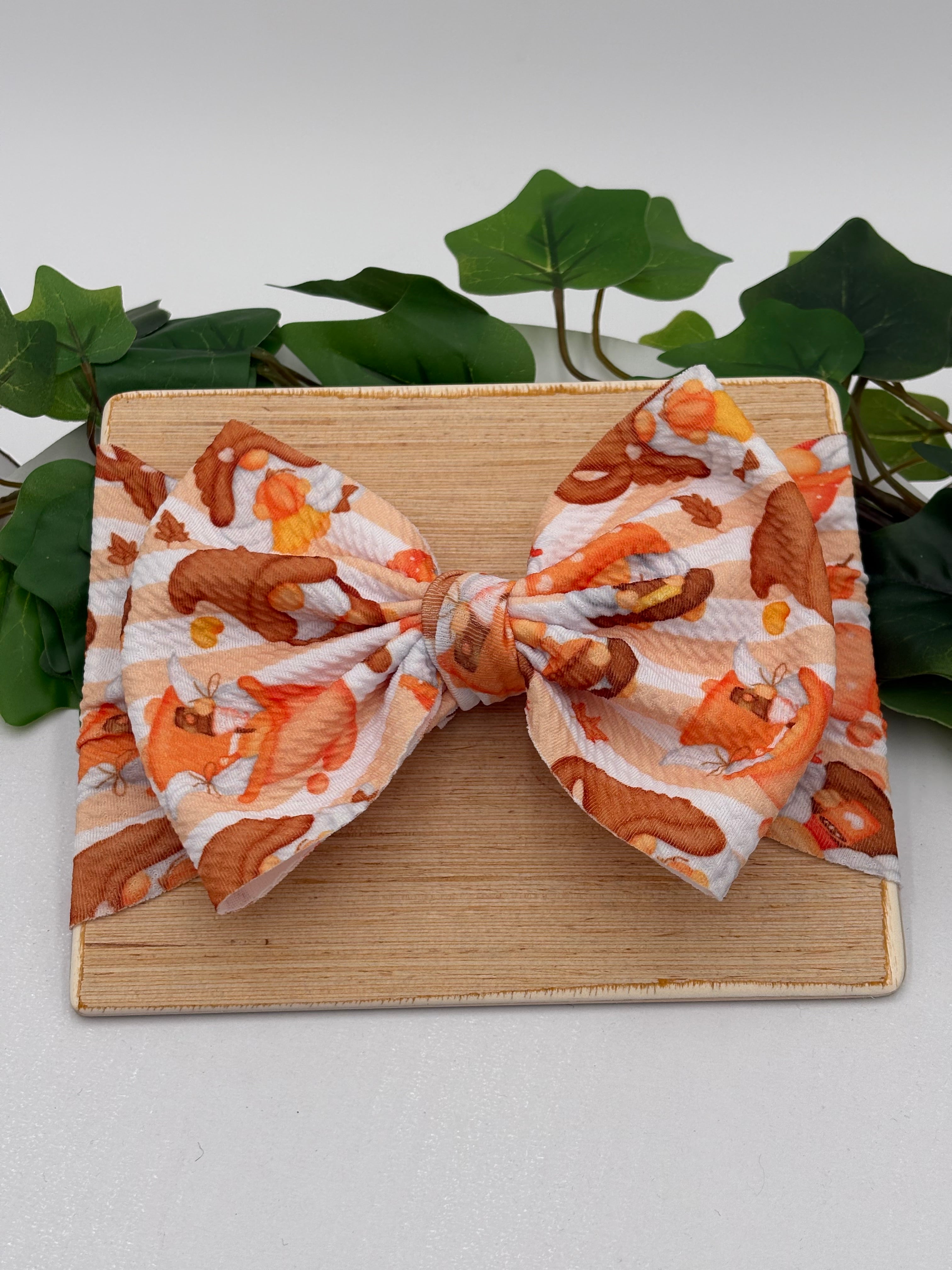 Autumn gnome themed big bow headband on a wooden board with a white background and greenery 