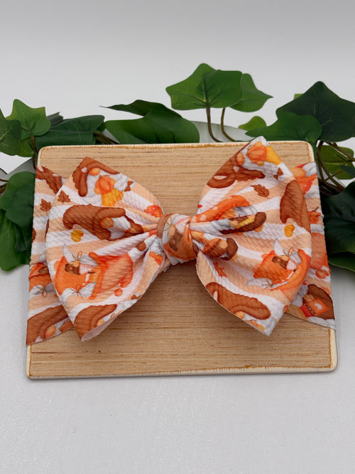 Autumn gnome themed big bow headband on a wooden board with a white background and greenery 