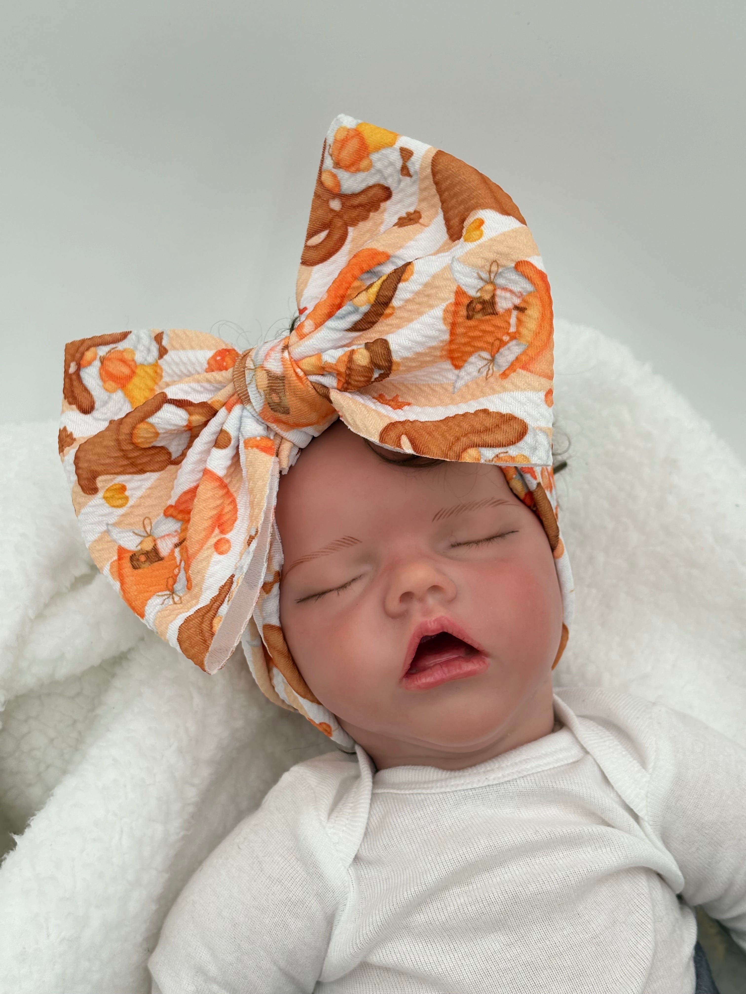 baby doll wearing a Autumn gnome themed big bow headband on a white background 