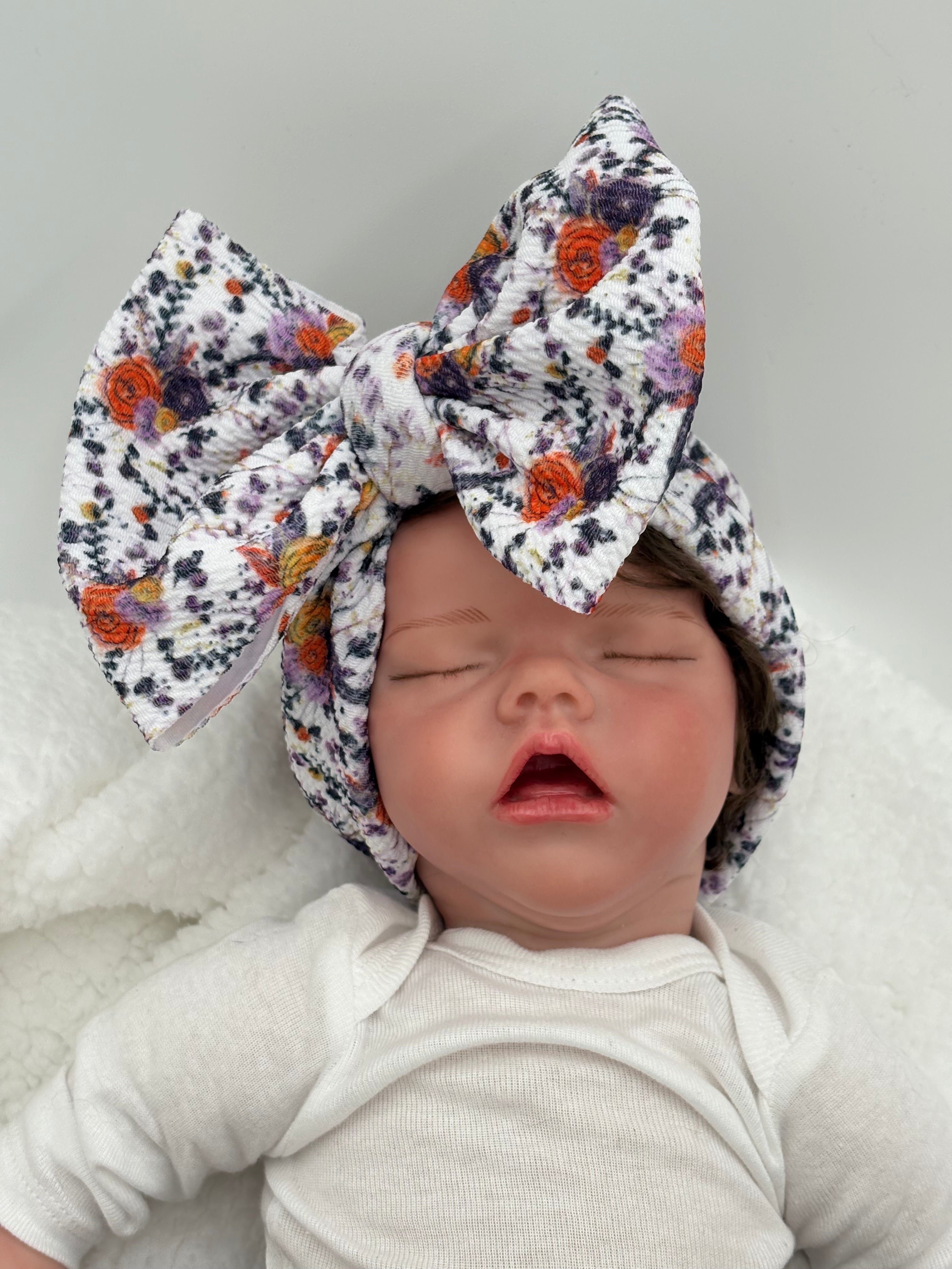 baby doll wearing a Autumn colored floral themed big bow headband on a white background 