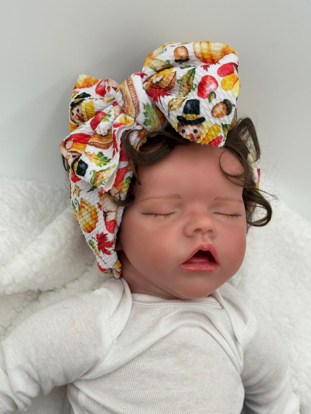 Baby doll wearing a Colorful thanksgiving themed big bow headband on a white background 
