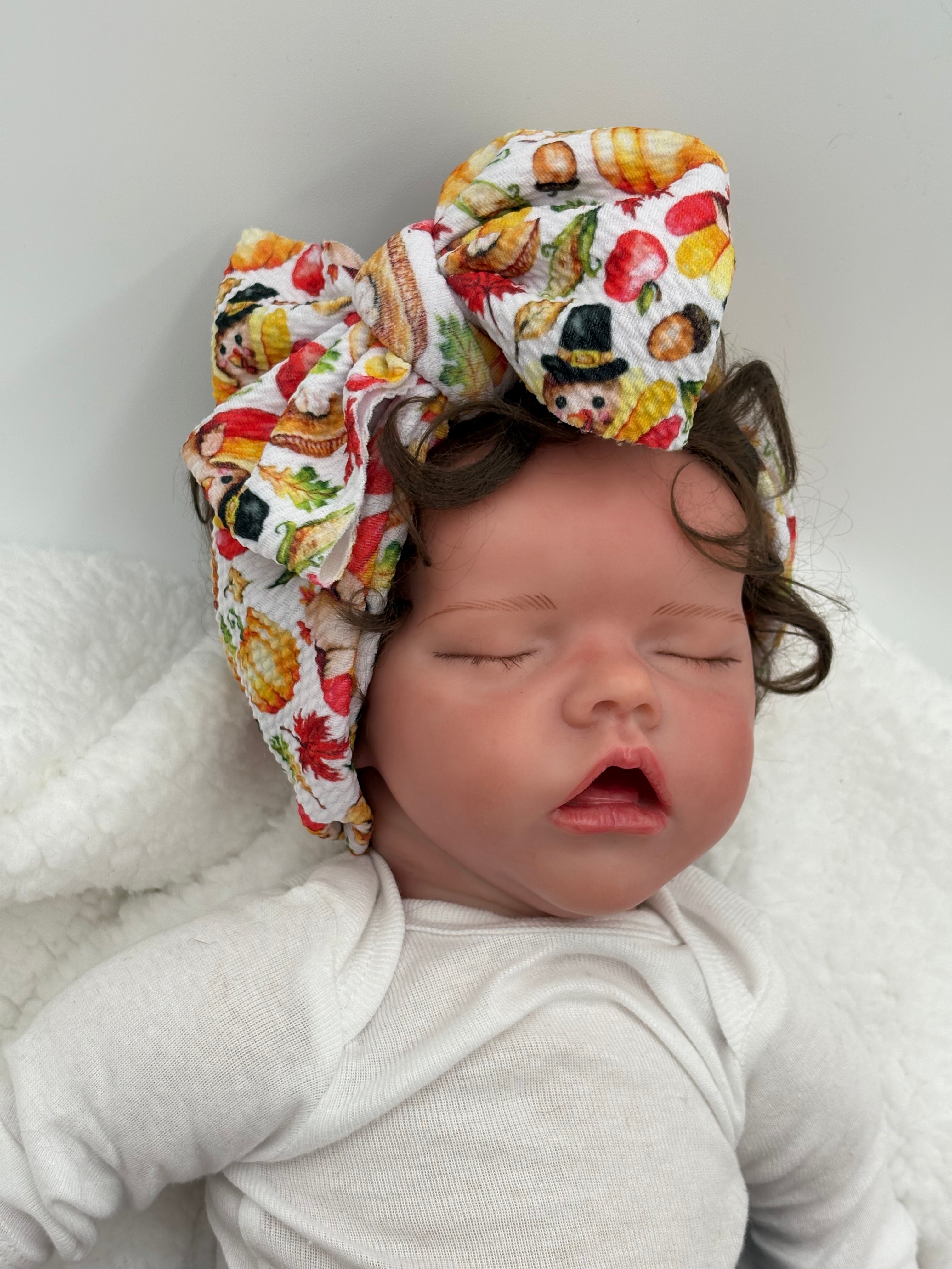 Baby doll wearing a Colorful thanksgiving themed big bow headband on a white background 