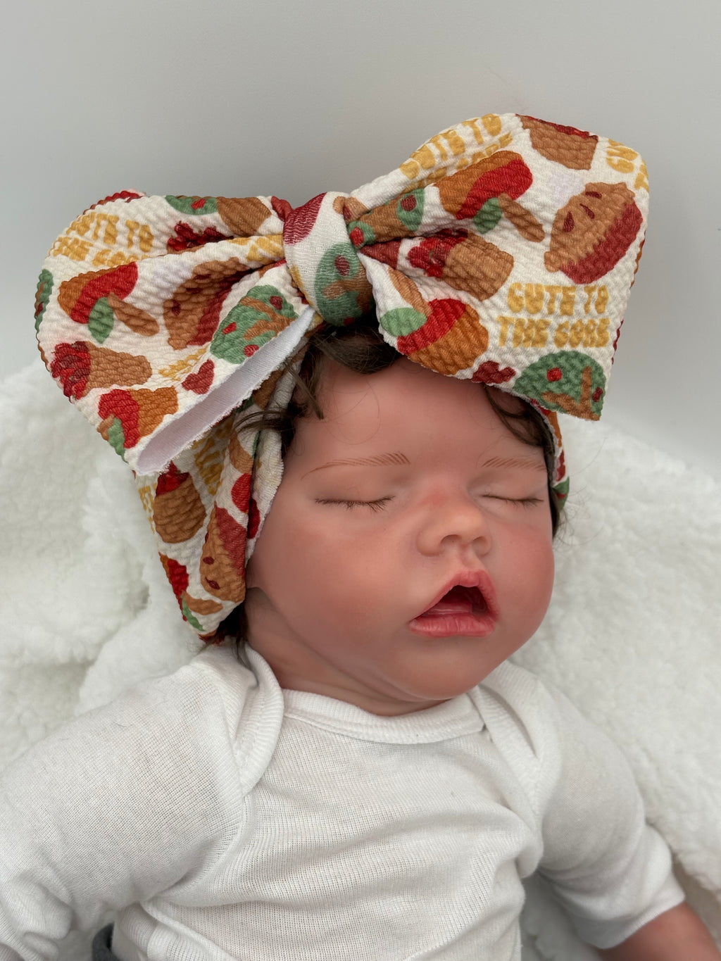 Baby doll wearing a Colorful Apple pie themed big bow headband on a white background 