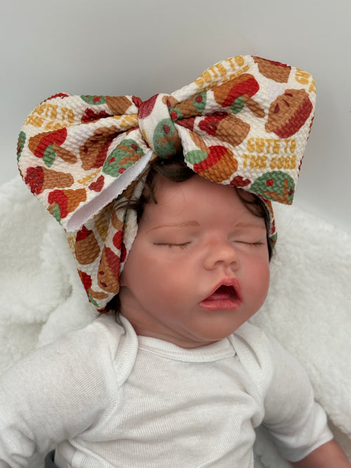 Baby doll wearing a Colorful Apple pie themed big bow headband on a white background 